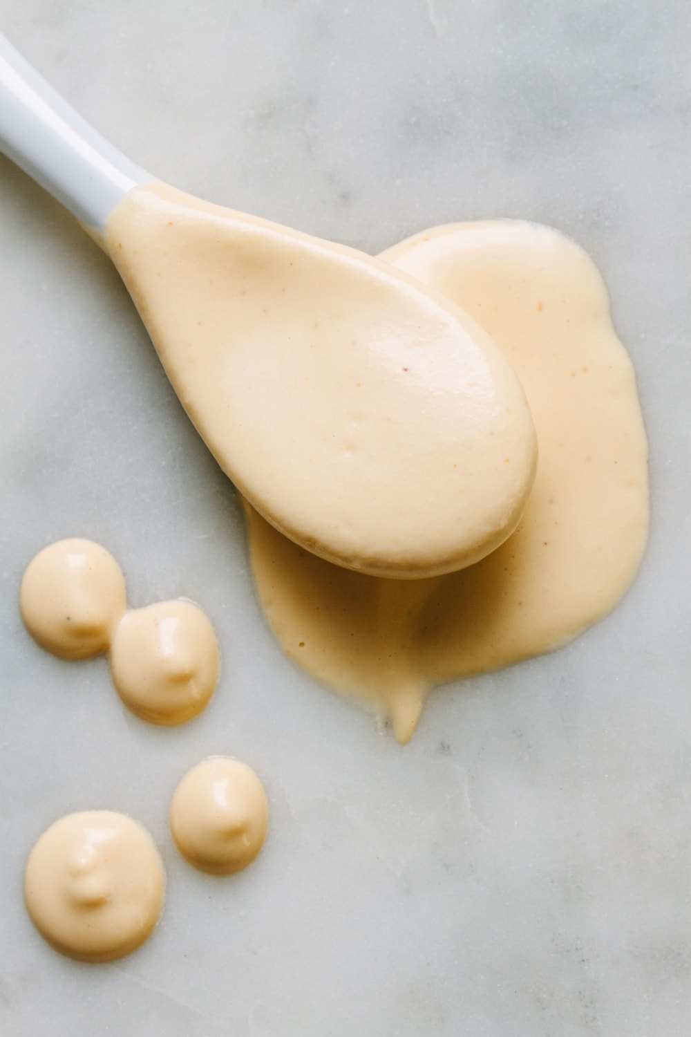 top down view of sriracha cashew cream sauce on a white ceramic spoon. 