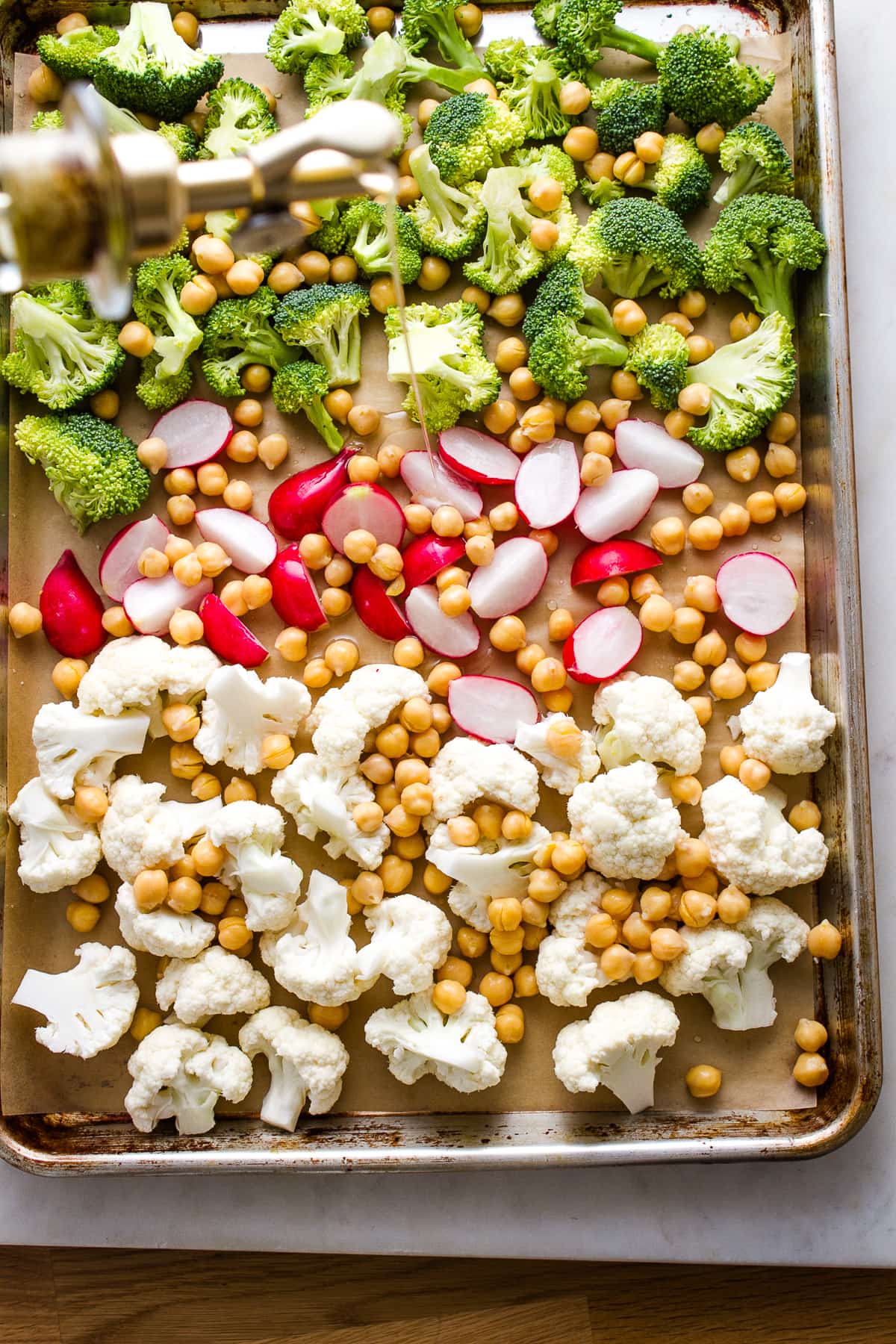 top down view of prepped veggies on a rimmed baking sheet being drizzled with olive oil.