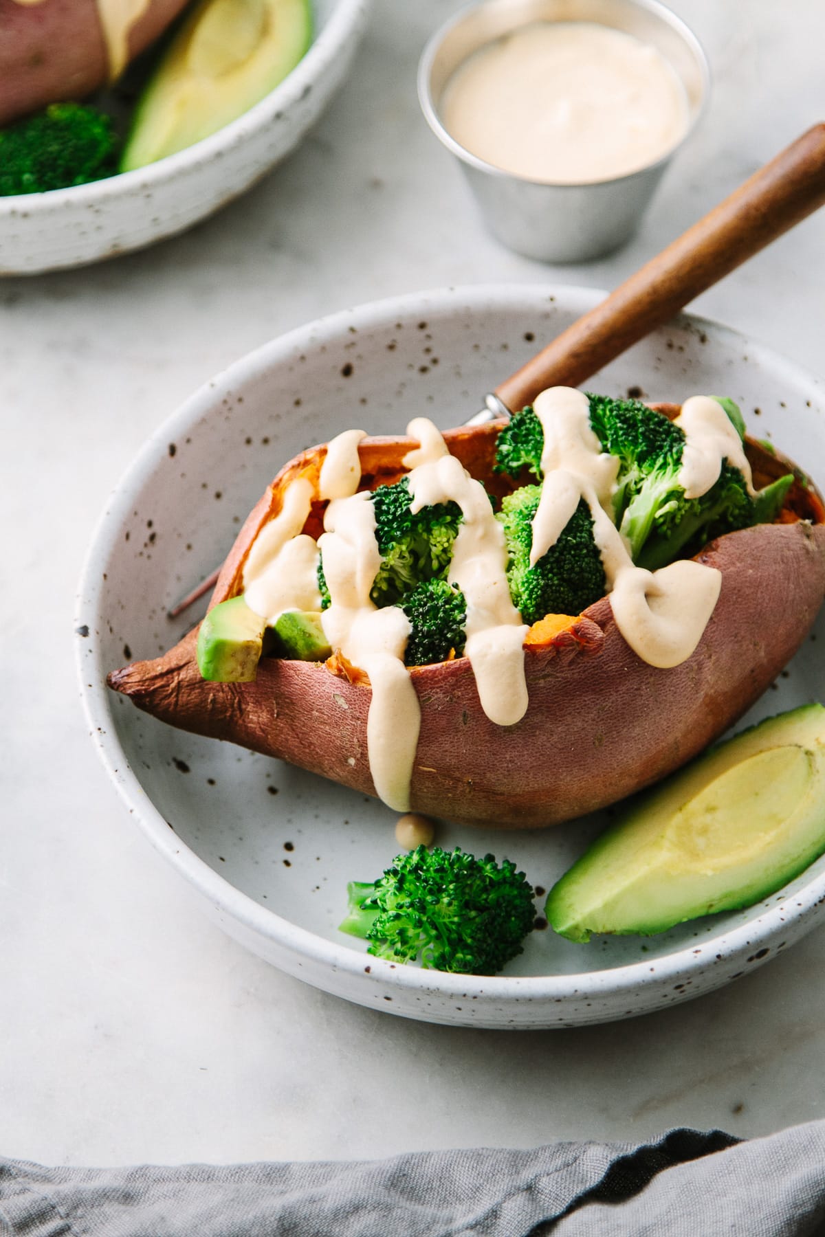 side angle view of stuffed baked sweet potatoes with broccoli, avocado and creamy spice cheese sauce in a bowl.