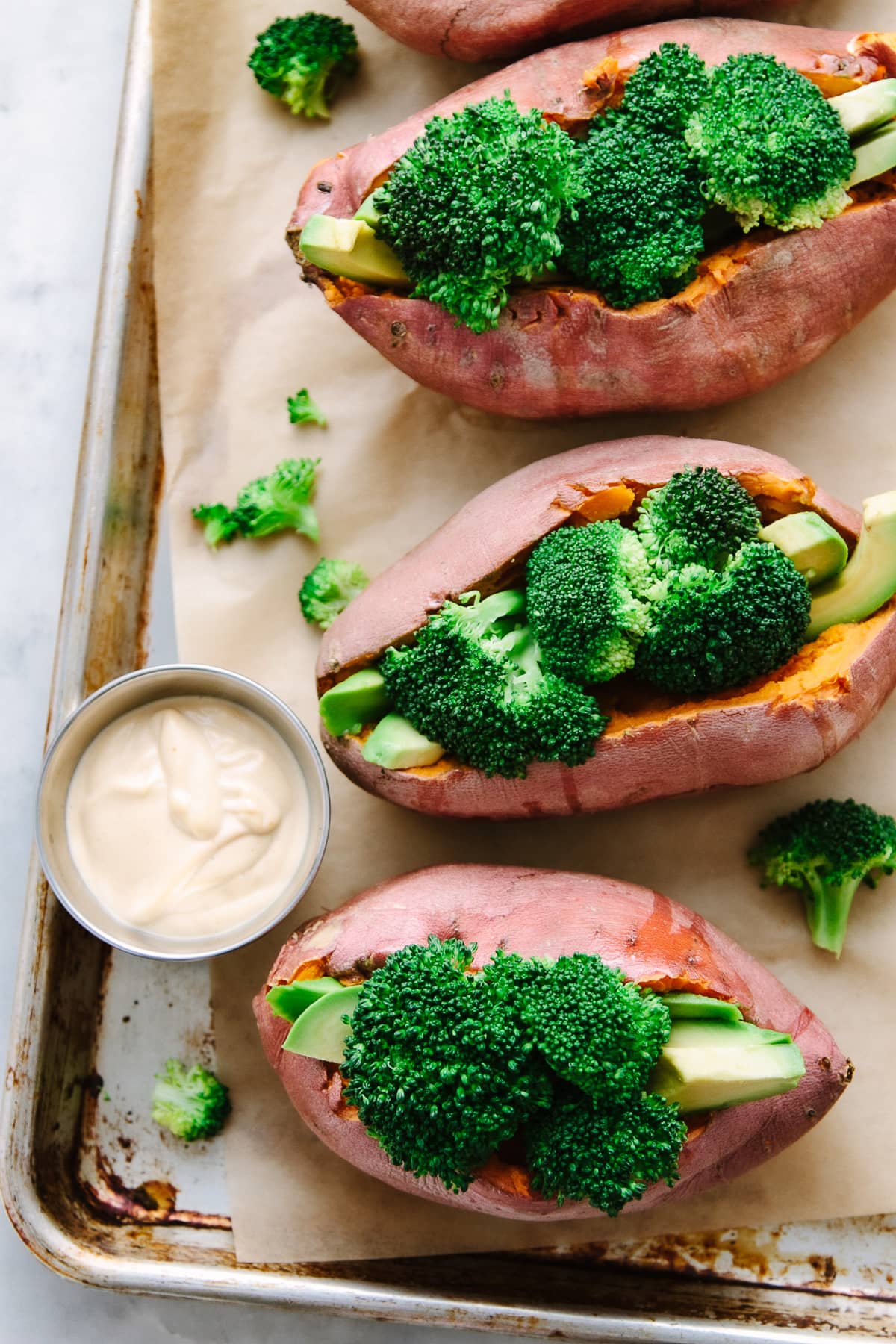 top down view of stuffed baked sweet potatoes with broccoli, avocado and creamy spice cheese sauce on a baking sheet.