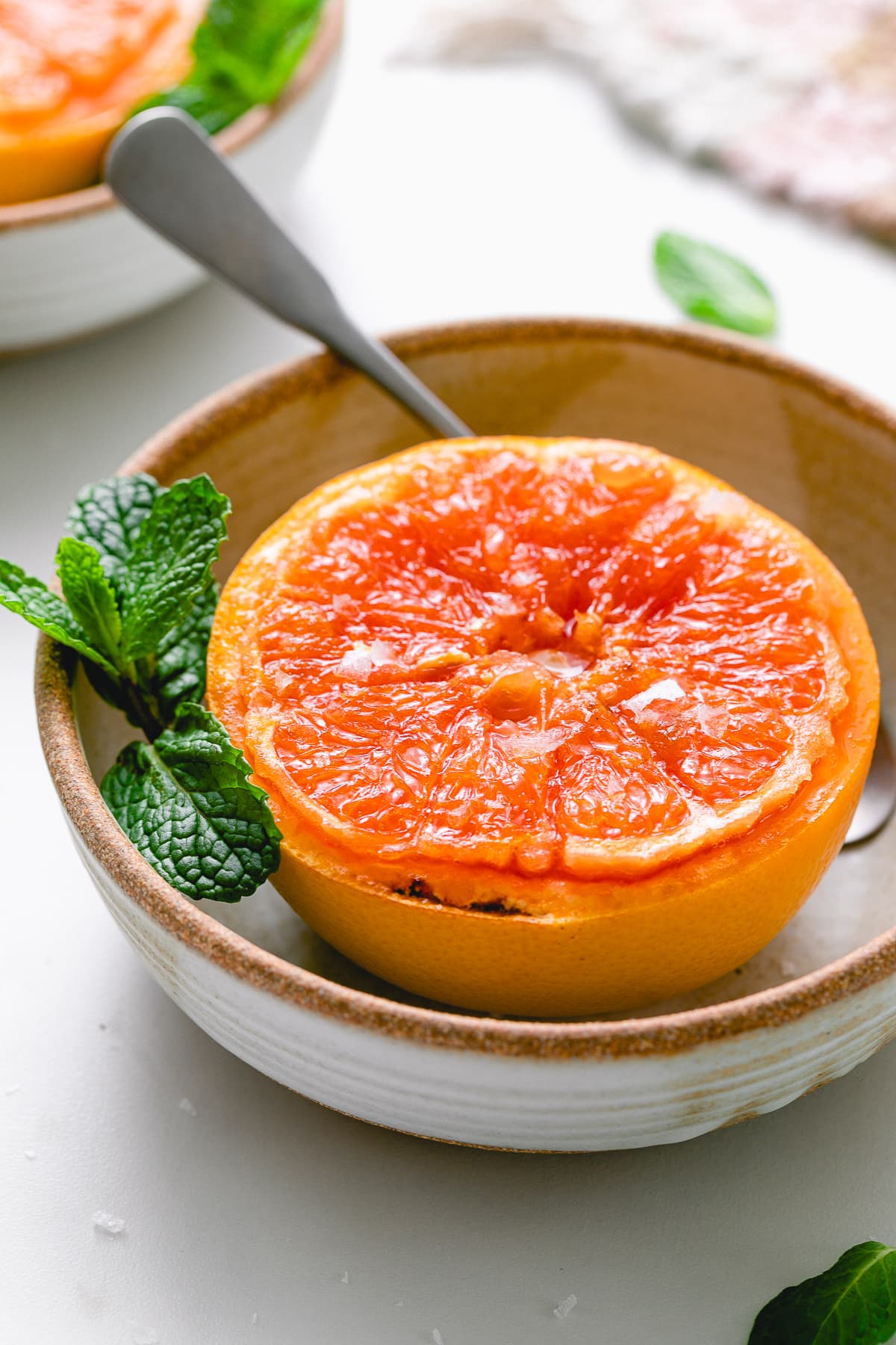 side angle view of broiled grapefruit in a bowl with spoon.