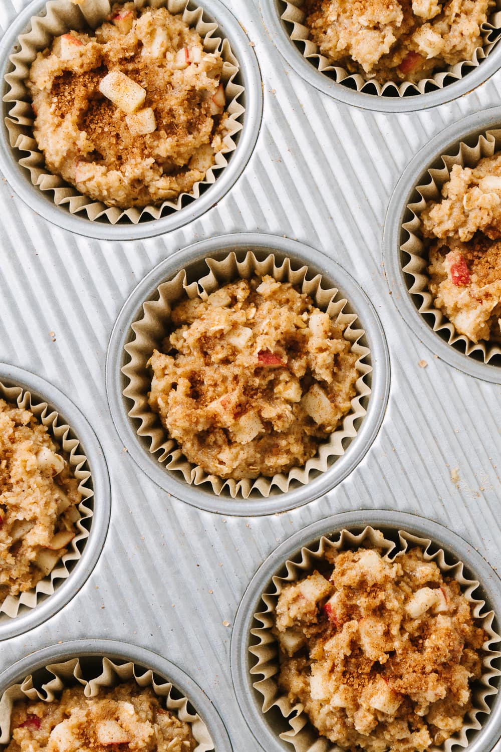 top down view of apple cinnamon muffin batter placed in lined muffin tin holes and sprinkled with cinnamon sugar before going into the oven