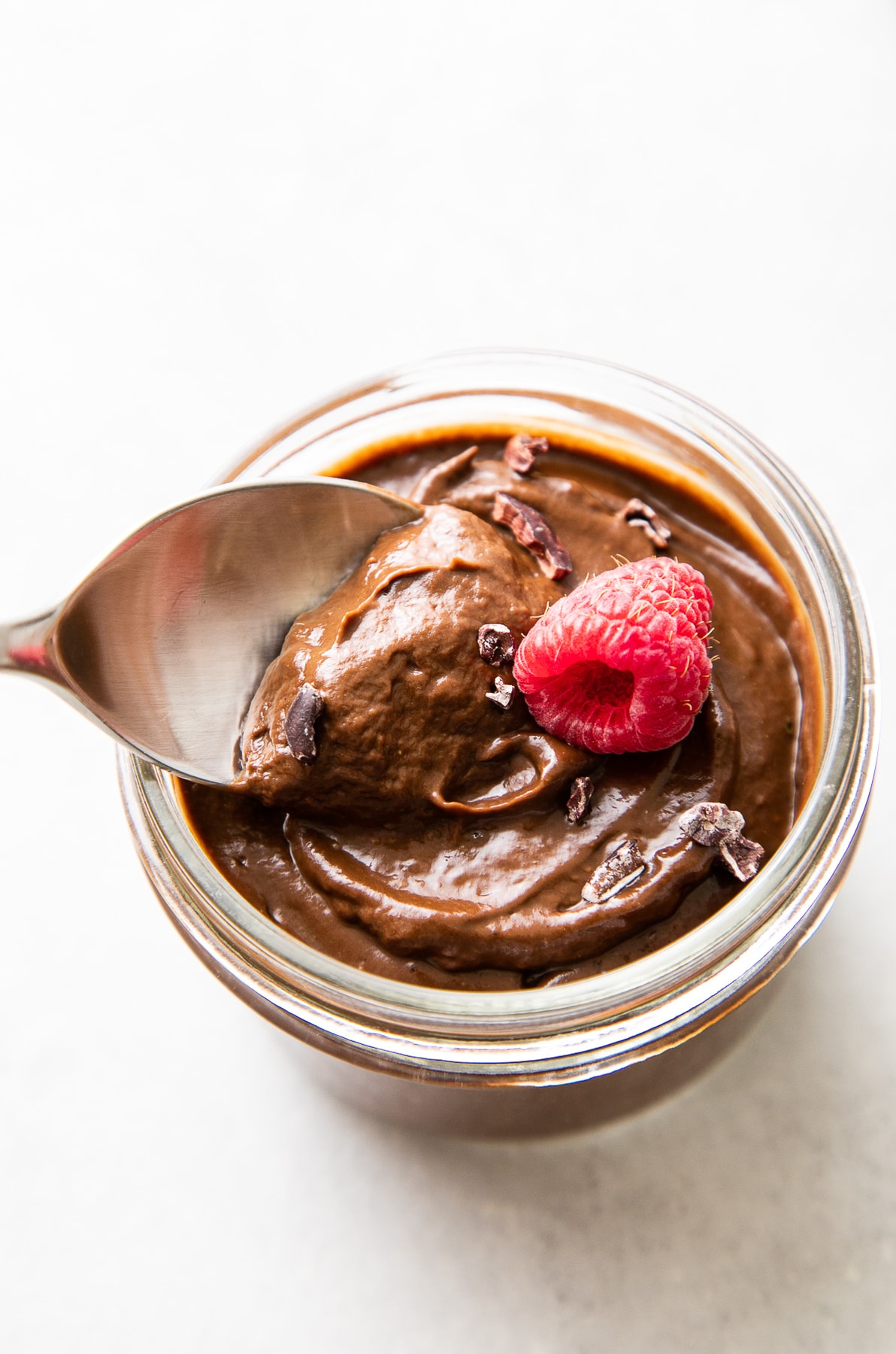 side angle view of spoon scooping up healthy raw chocolate avocado pudding in glass jar.