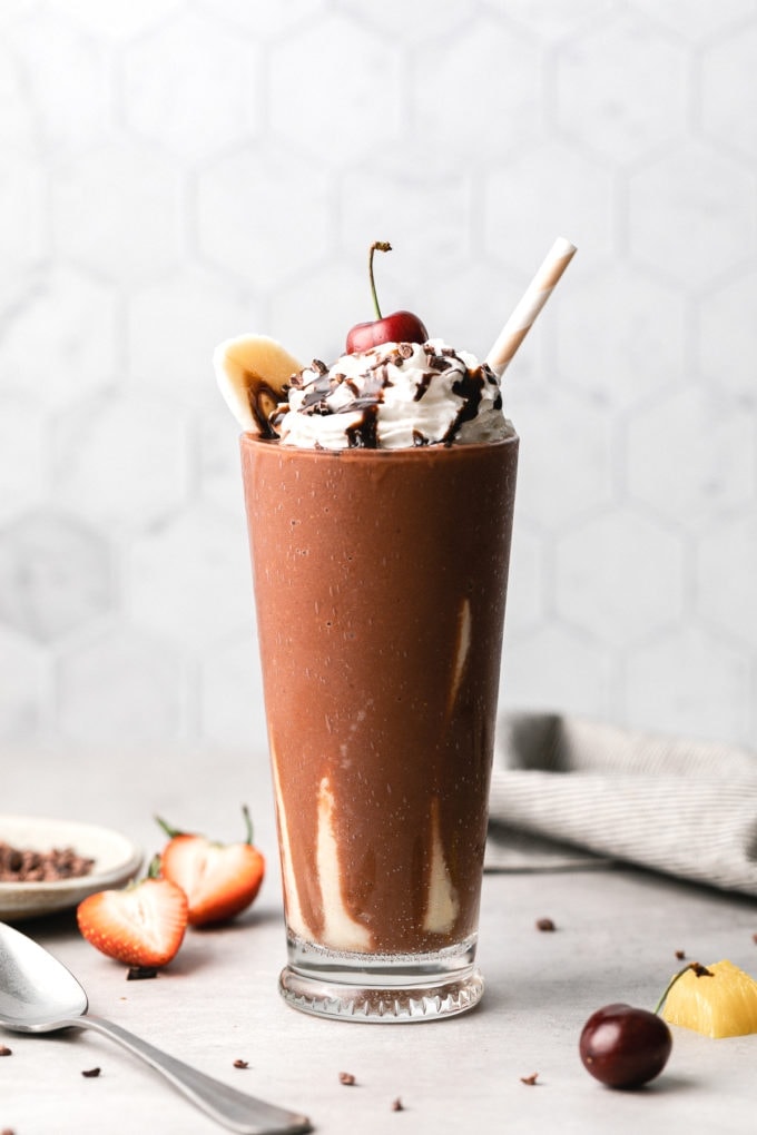head on view of banana split smoothie in a glass with straw.