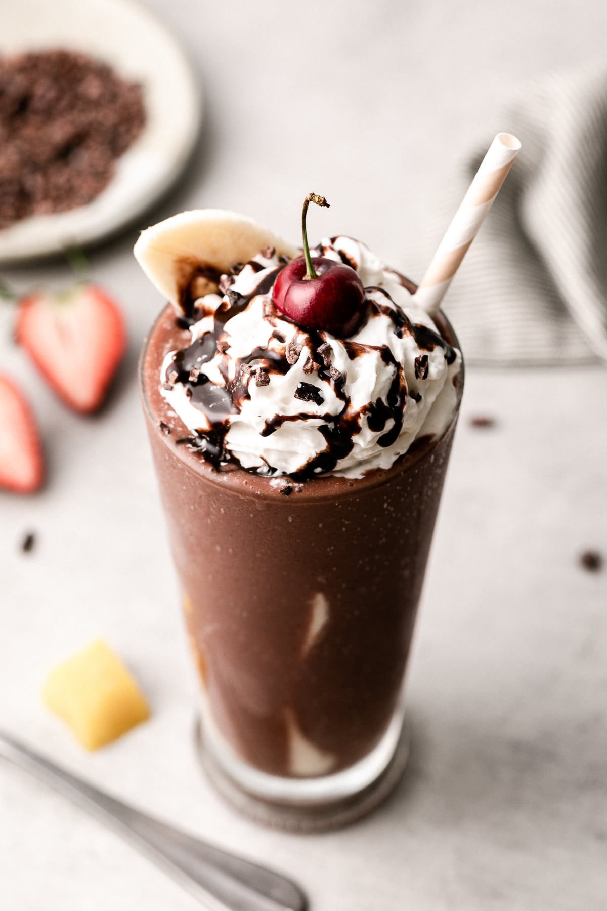 side angle view of banana split smoothie in a glass with straw.