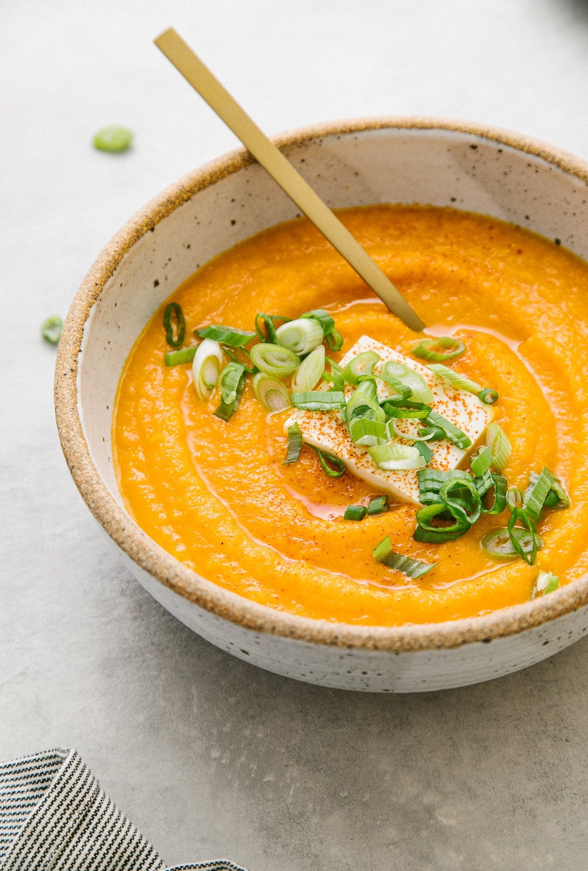 side angle view of carrot miso soup in a bowl with gold spoon.