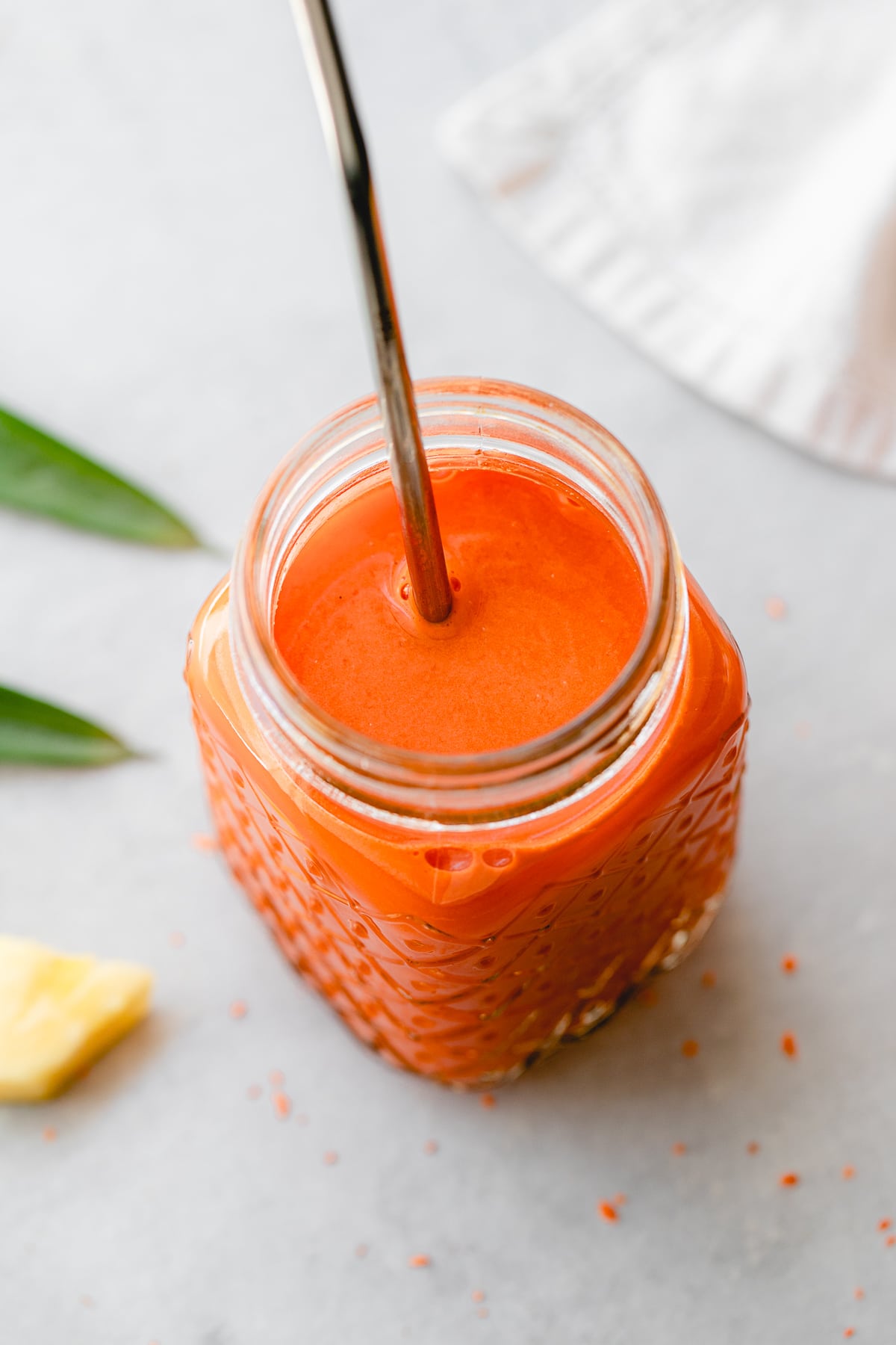side angle view of carrot pineapple juice with ginger in a glass with straw.