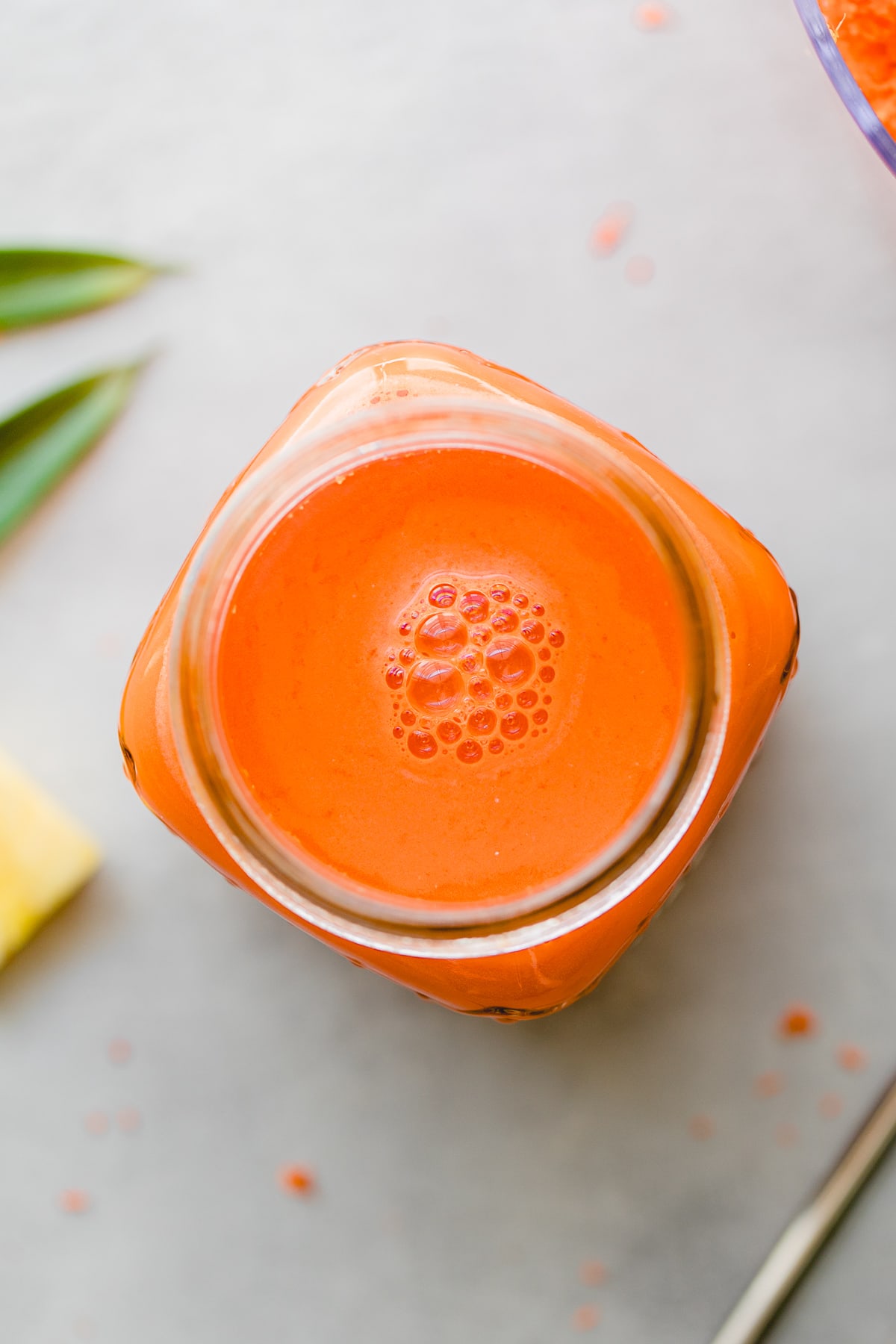 top down view of carrot pineapple juice with ginger in a glass with items surrounding
