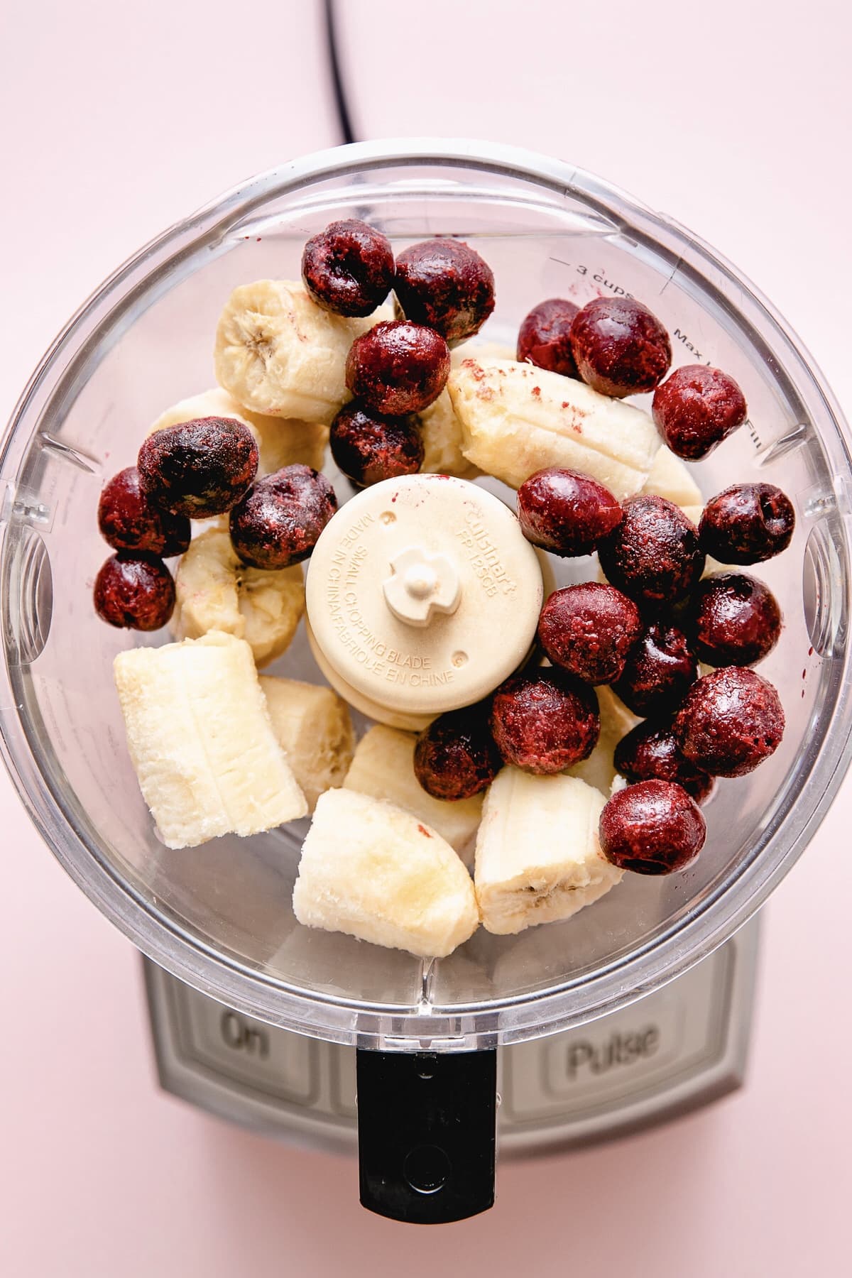 top down view of banana and cherries added to food processor.