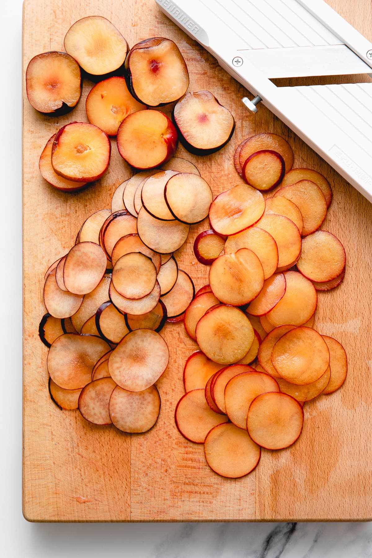 top down view of sliced plums on wooden cutting board.