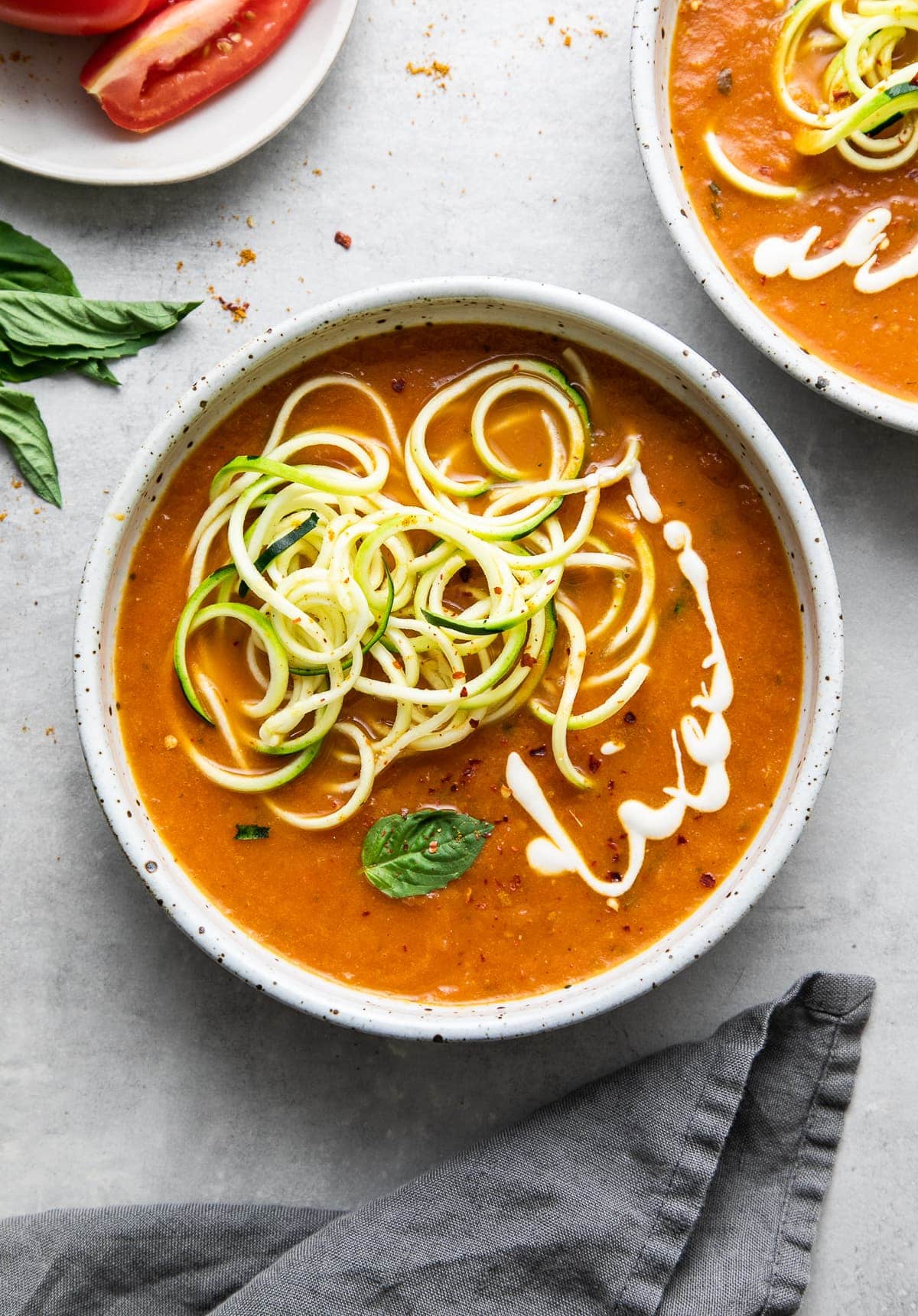 top down view of spicy tomato soup with curry and zucchini noodles in a bowl with items surrounding.