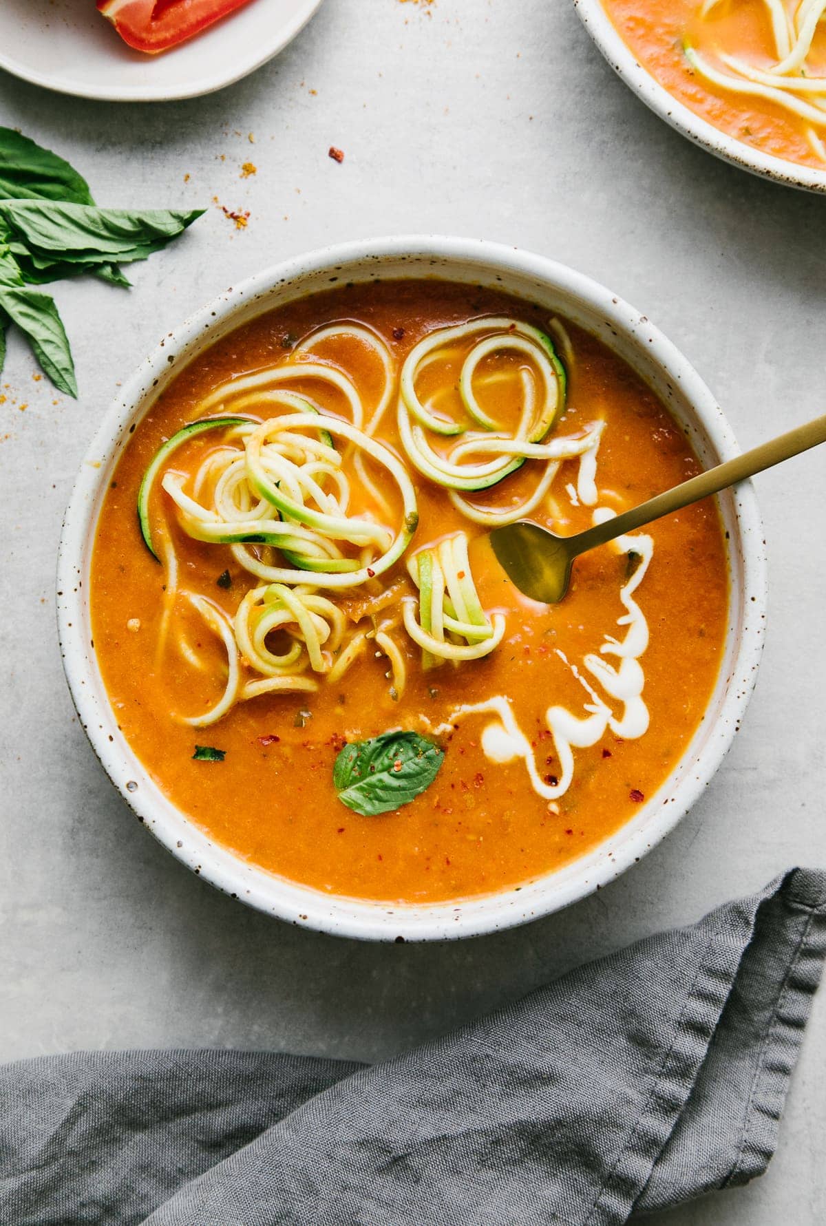 top down view of spicy tomato soup with curry and zucchini noodles in a bowl with items surrounding.