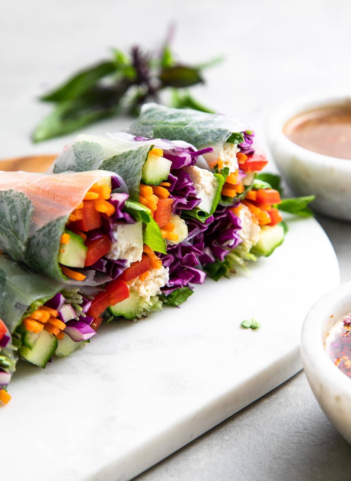 side angle view of sliced summer rolls on a marble serving board with items surrounding.