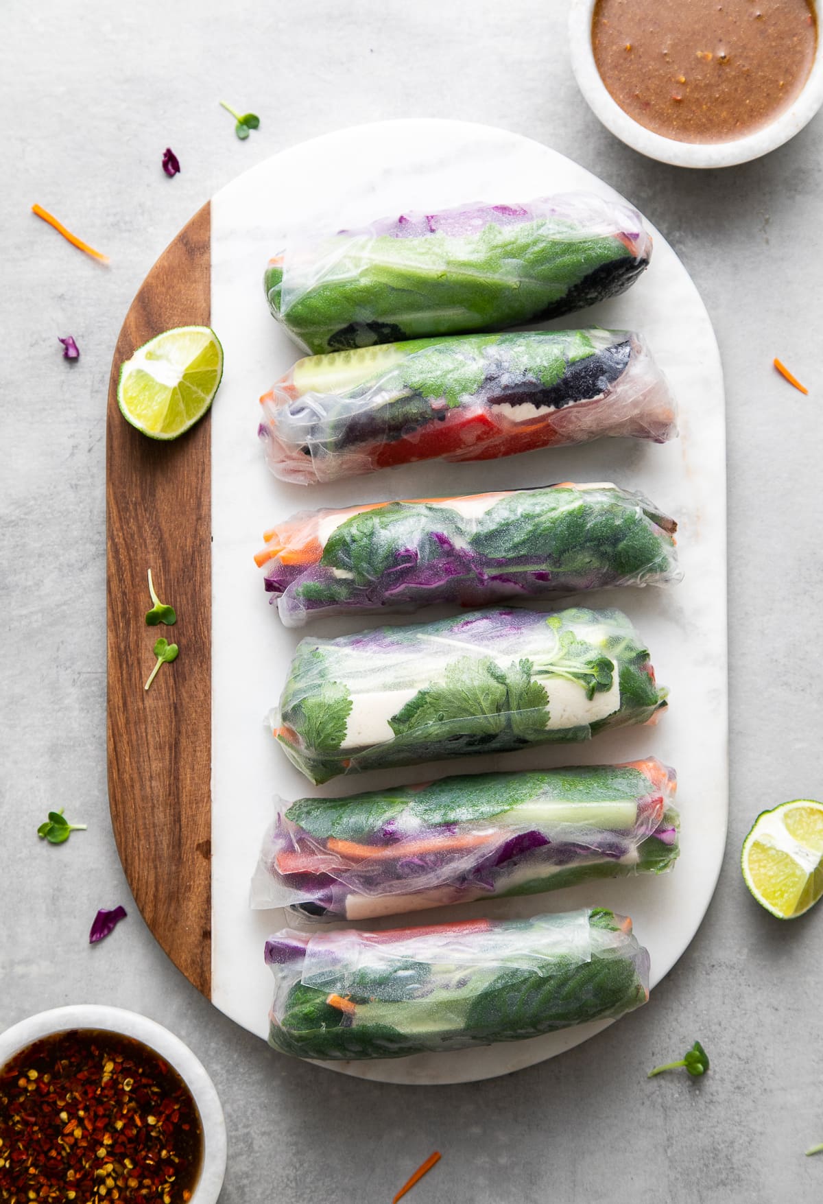top down view of summer rolls on a marble serving board with dipping sauces.