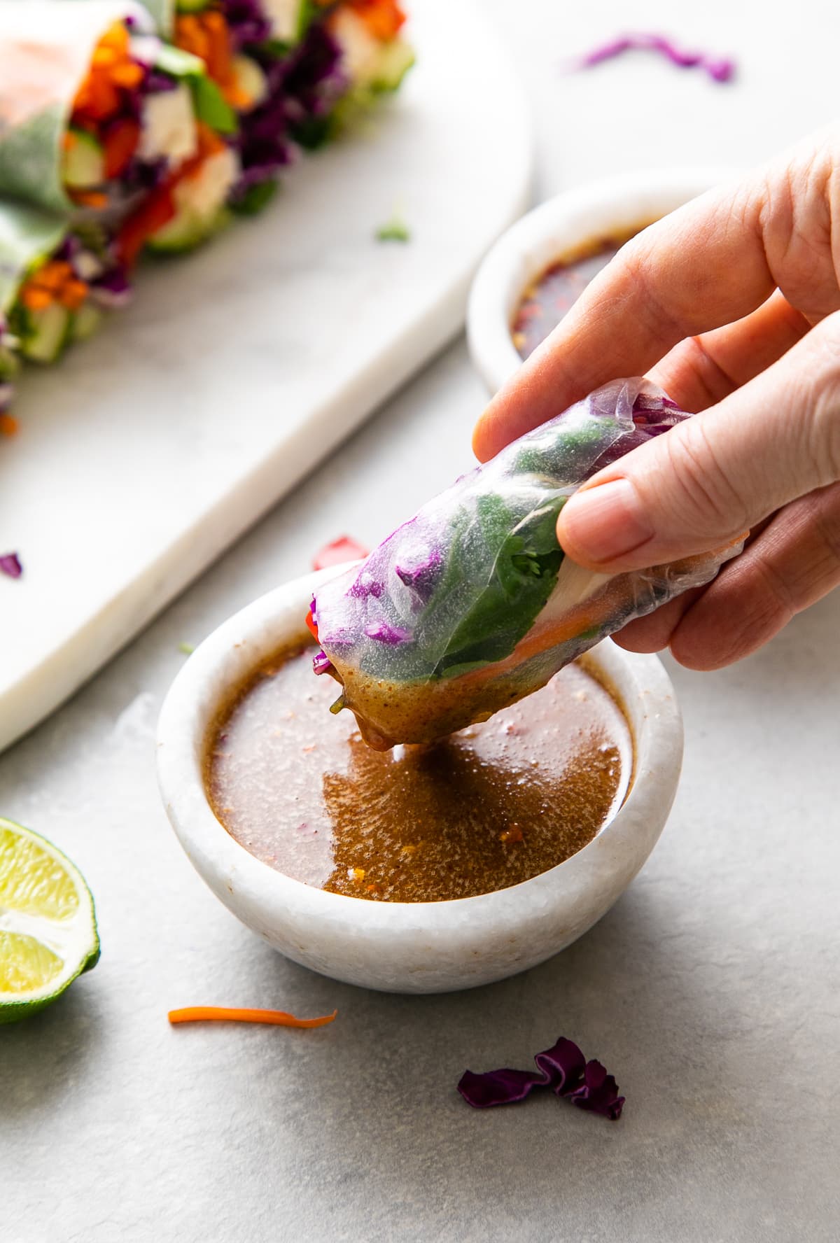 side angle of summer roll dipped in peanut dipping sauce with items surrounding.
