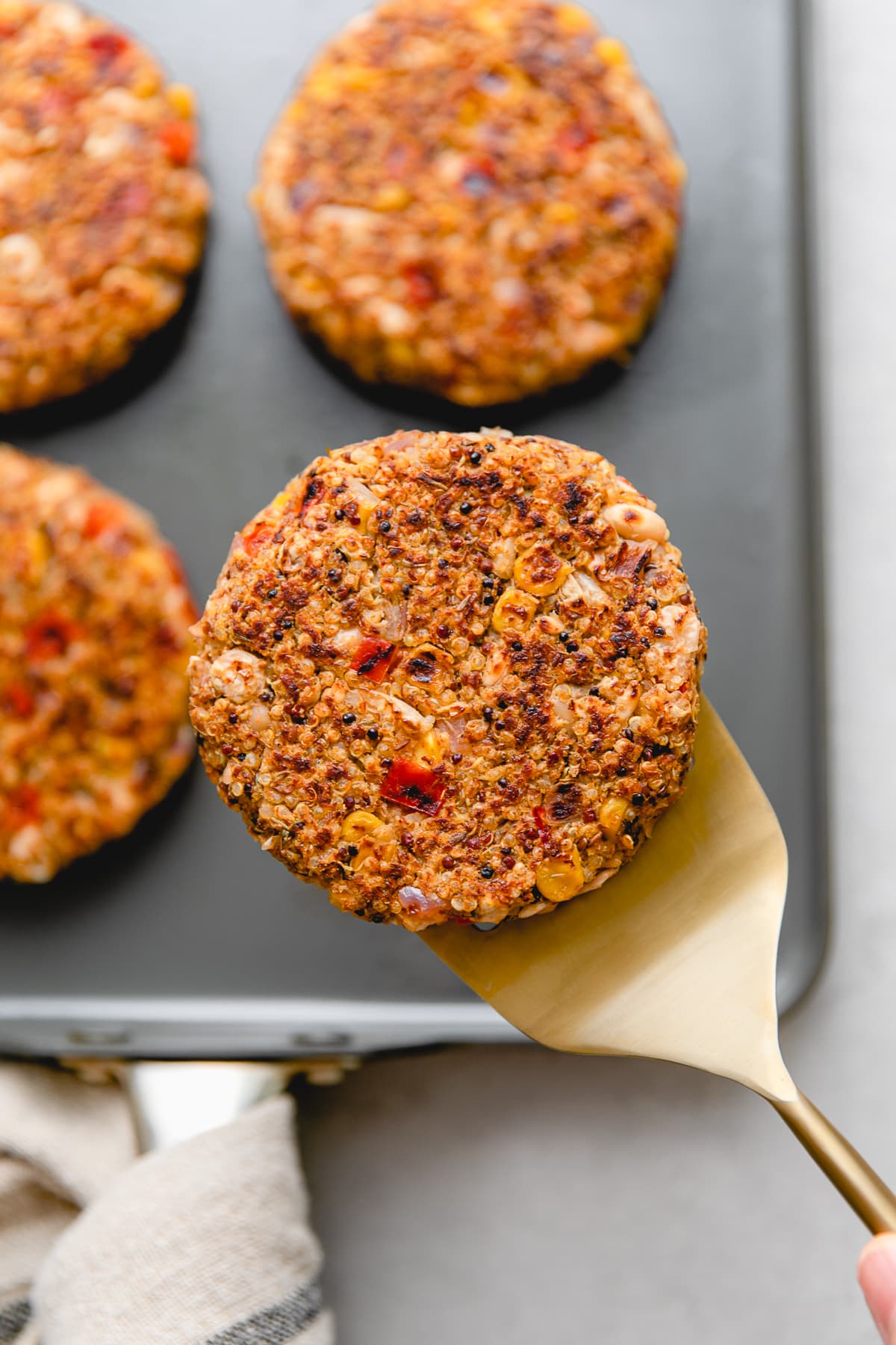 top down view of quinoa and white bean veggie burger patty resting on a spatula with items in the background.