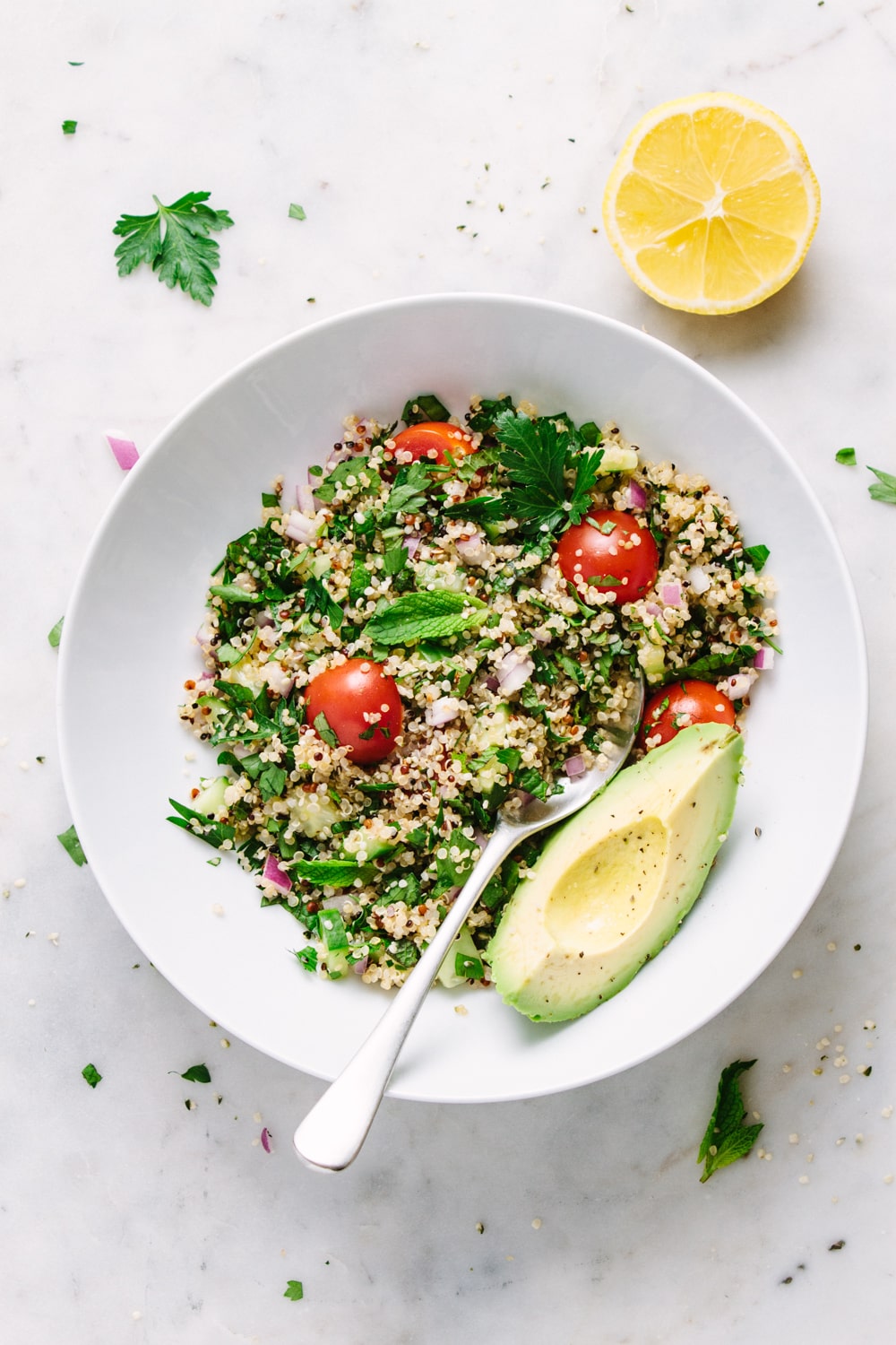 side angle view of a white bowl with serving of healthy quinoa tabbouleh with hemp hearts and avocado.