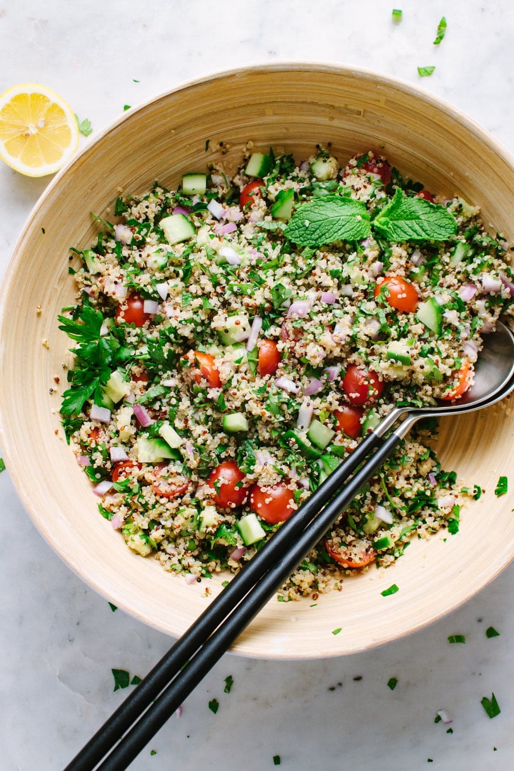 top down view quinoa tabbouleh freshly mixed in a large mixing bowl with serving utensils.