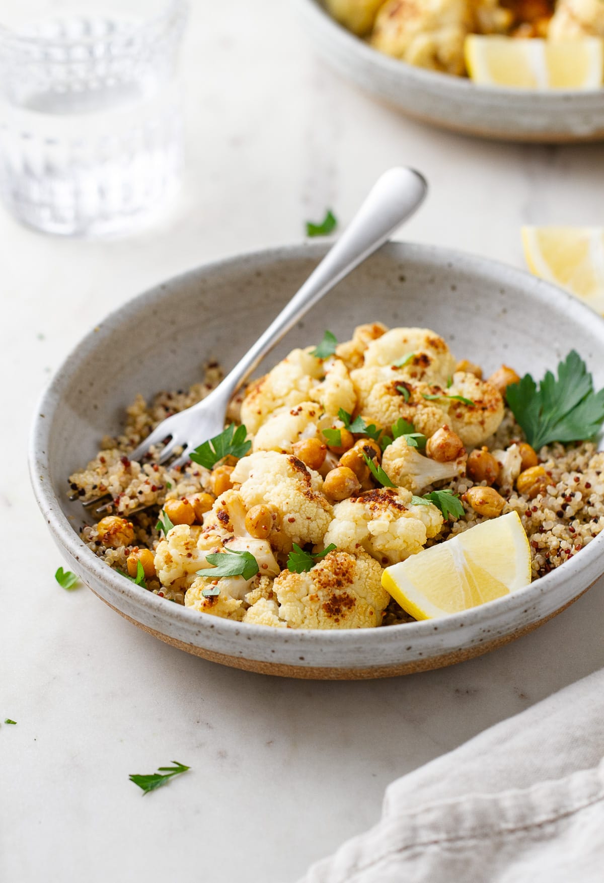 side angle view of a bowl with a serving of quinoa, roasted cauliflower with mustard dressing and chickpeas.