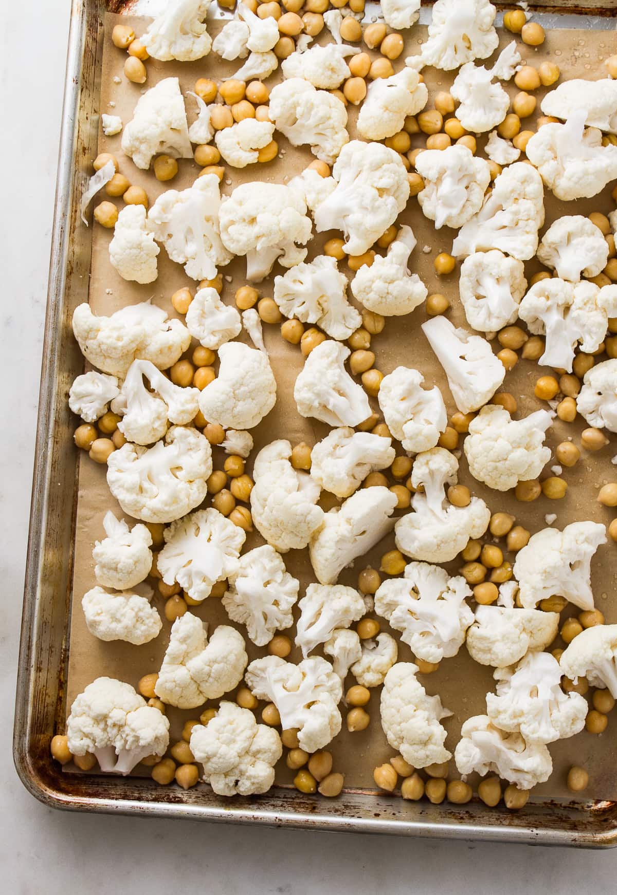 top down view of cauliflower florets and chickpeas on a rimmed baking sheet before roasting.