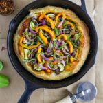 top down view of vegetarian cast iron skillet pizza with items surrounding.