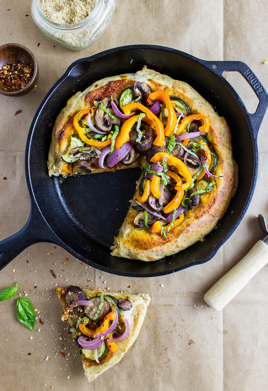 top down view of veggie cast iron skillet pizza with slice cut and items surrounding.