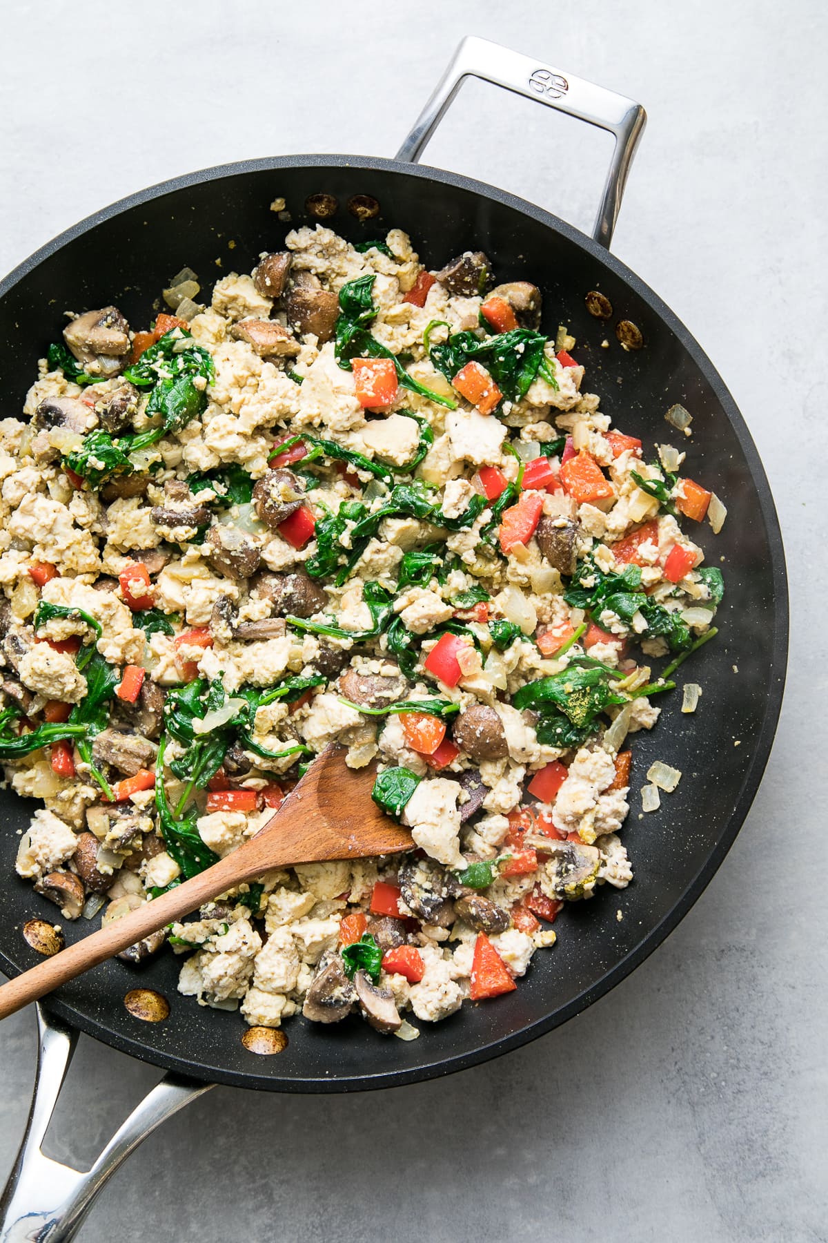 top down view of veggie filled tofu scramble in a skillet with wooden spoon.