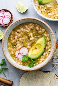 top down view of bowl filled with white bean tomatillo soup with items surrounding.
