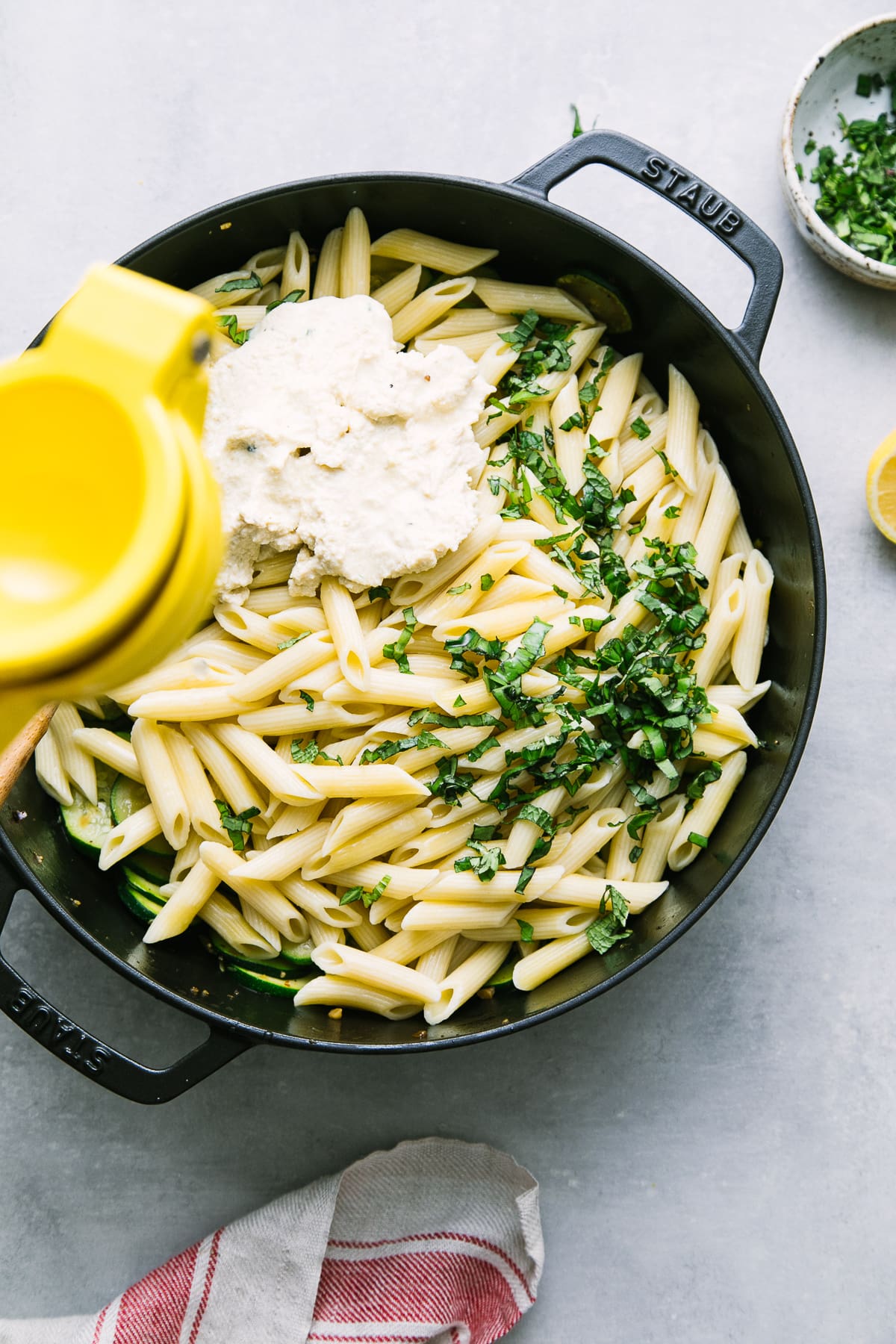 top down view showing the process of adding lemon juice to pasta, zucchini and vegan ricotta in a pan.