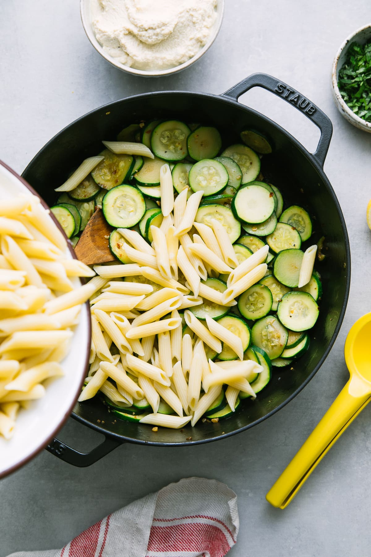 top down view showing the process of adding pasta to a pot of cooked zucchini.