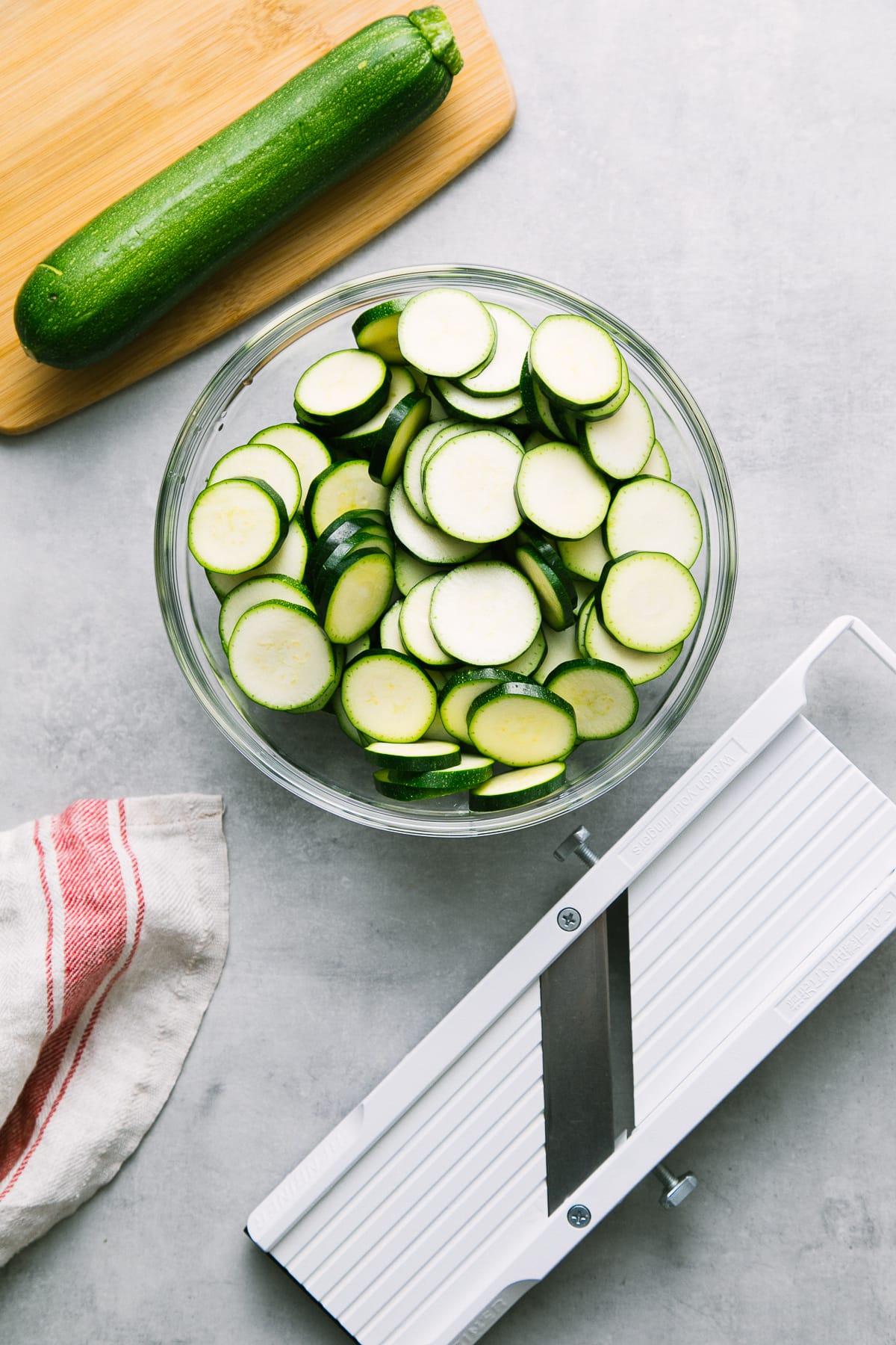 top down view of sliced zucchini in a bow with items surrounding.