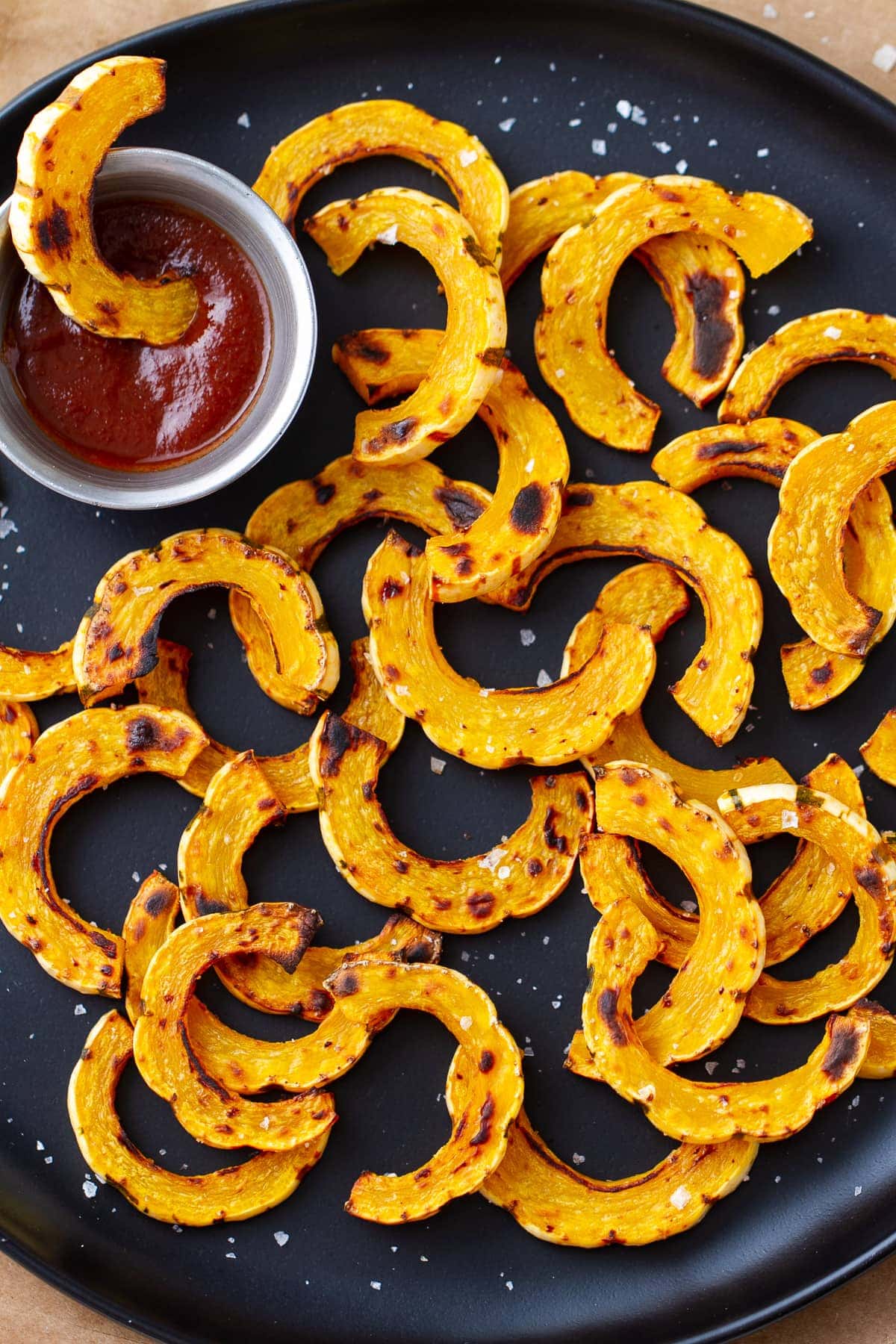 top down view of a black plate full of delicata squash fries with sriracha.