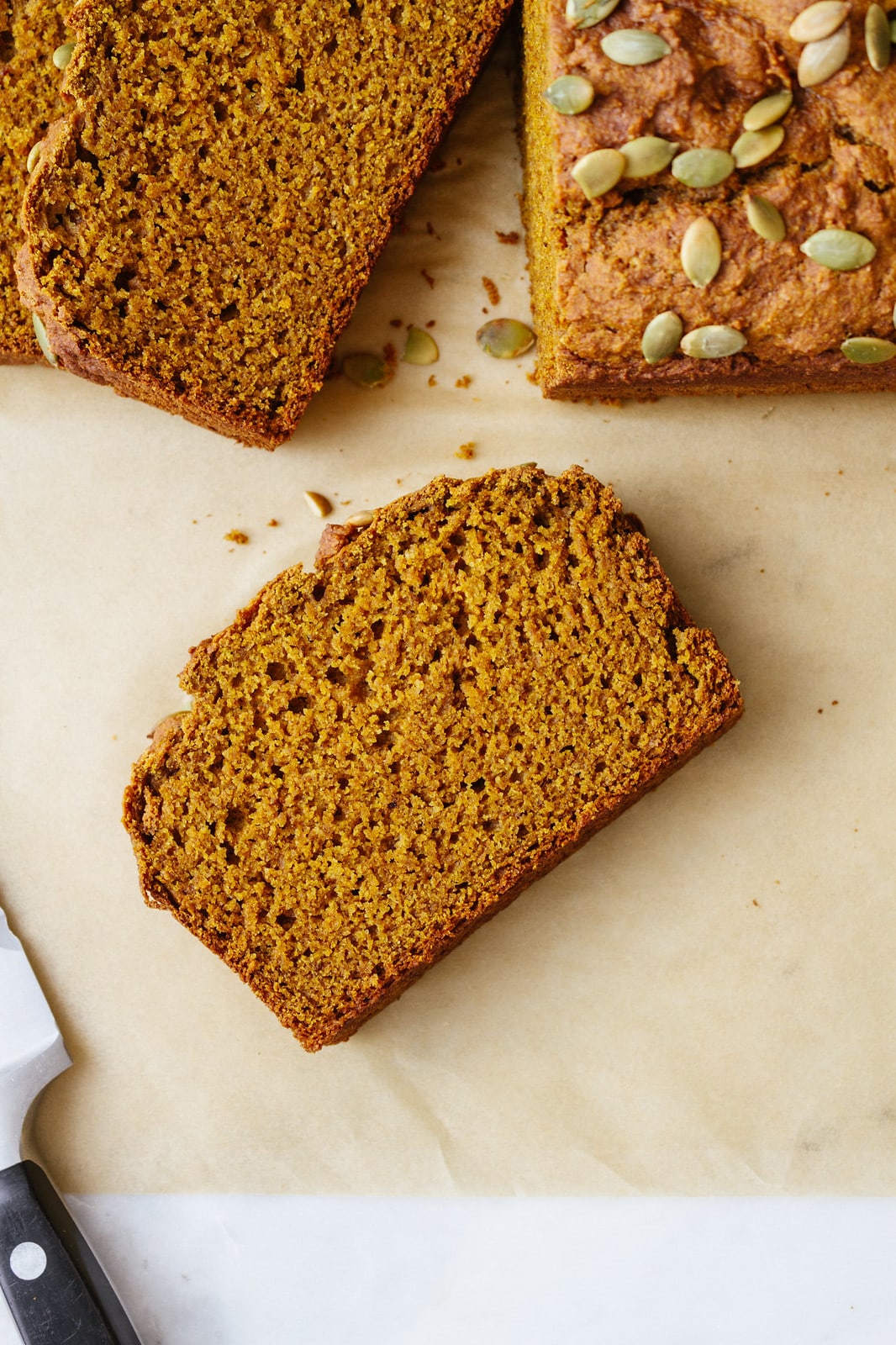 top down view of slice of vegan pumpkin bread on parchment paper with items surrounding.