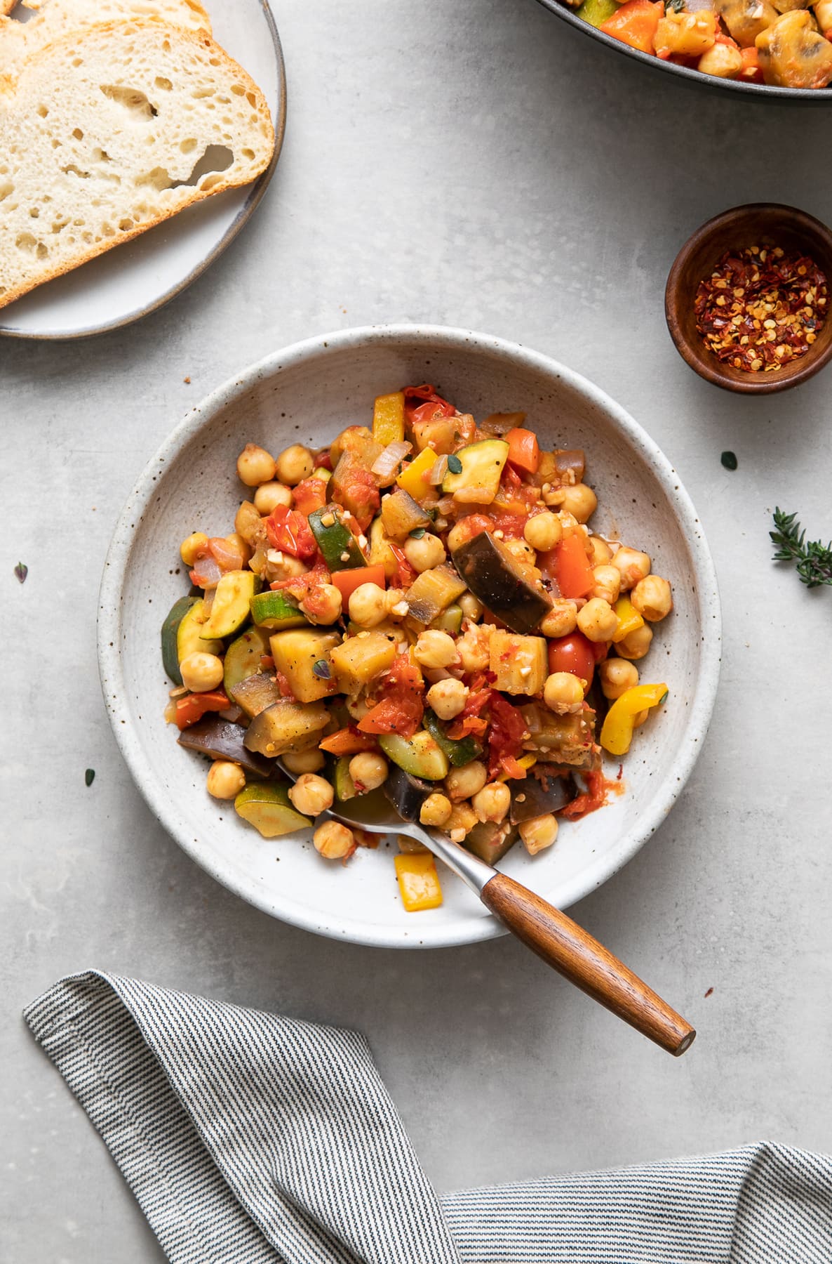 top down view of a bowl with serving of chickpea ratatouille with wooden fork and items surrounding.