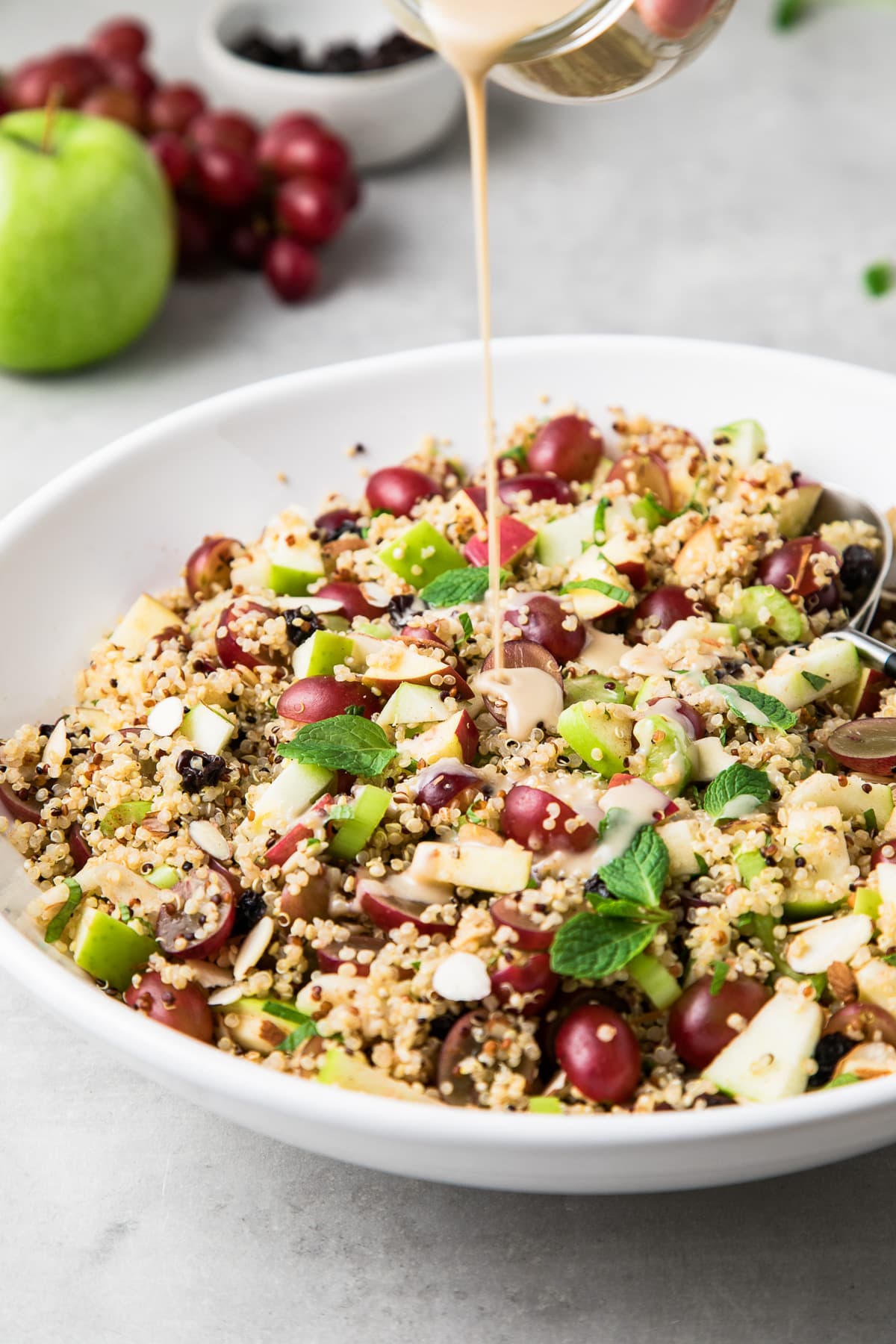 side angle view of sweet tahini dressing being poured over apple quinoa salad.