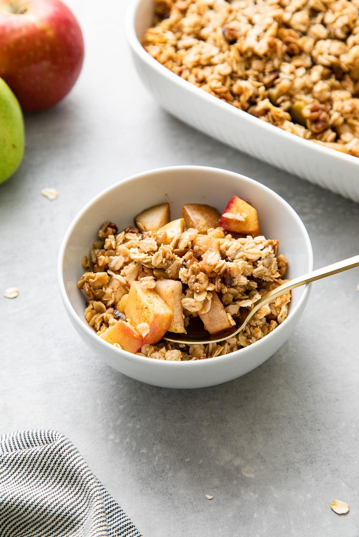 side angle view of vegan apple pear crisp in a white serving bowl with items surrounding.