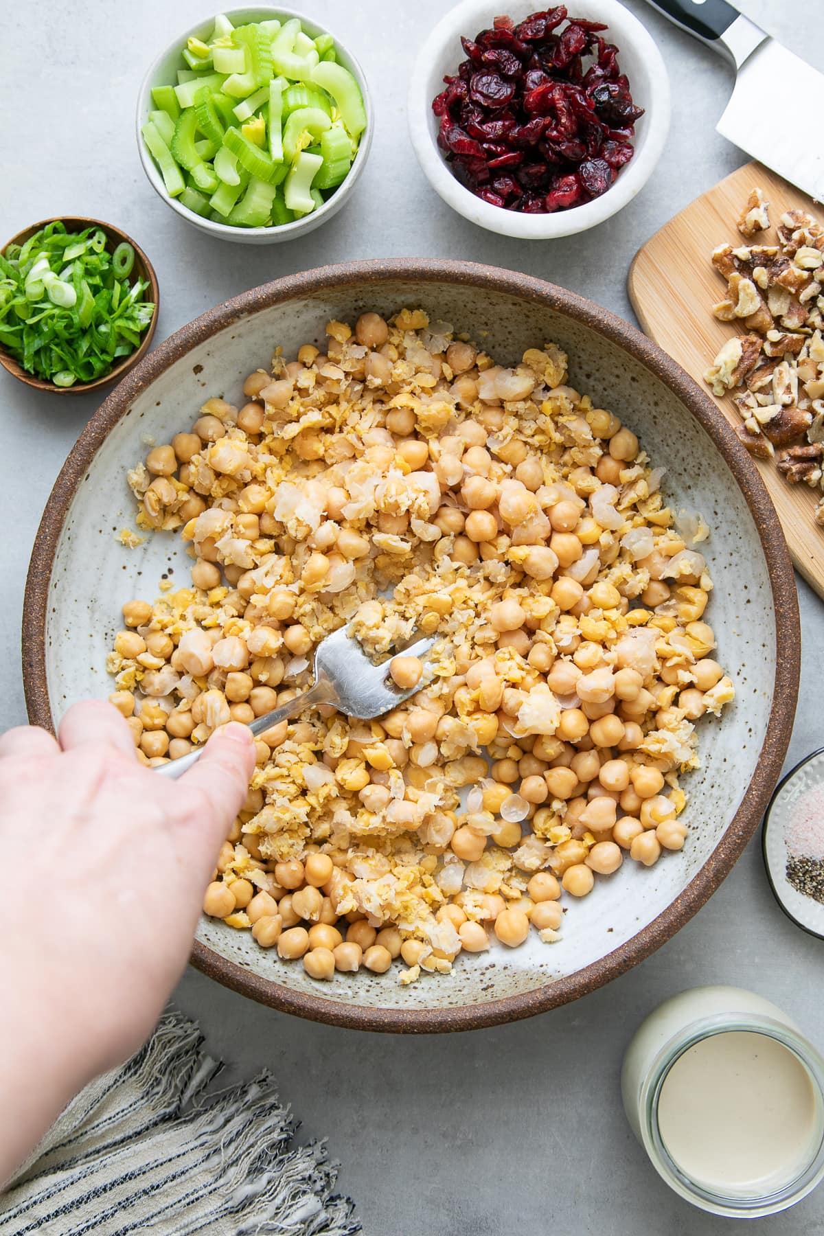 top down view showing the process of mashing chickpeas in a bowl with items surrounding.