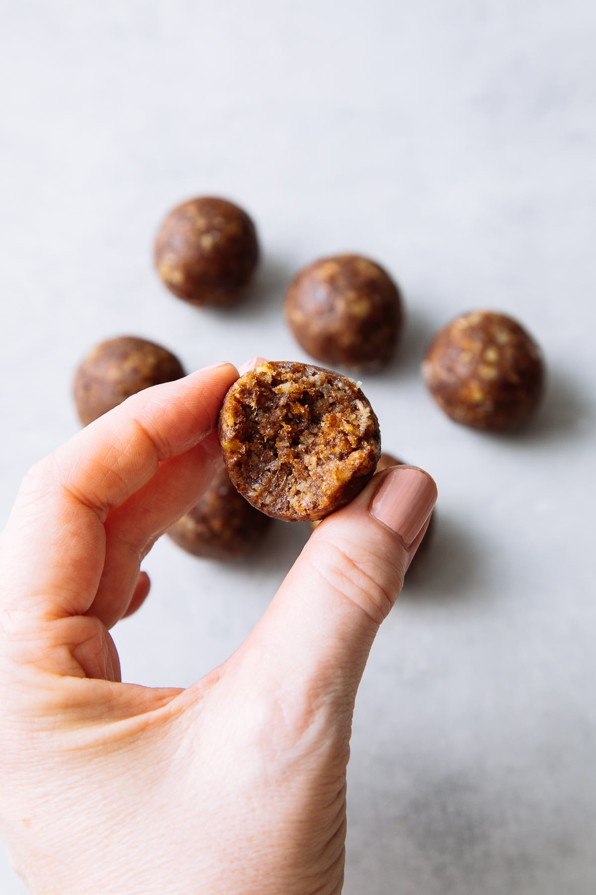 hand holding raw pecan pie energy ball with bite taken showing the center.