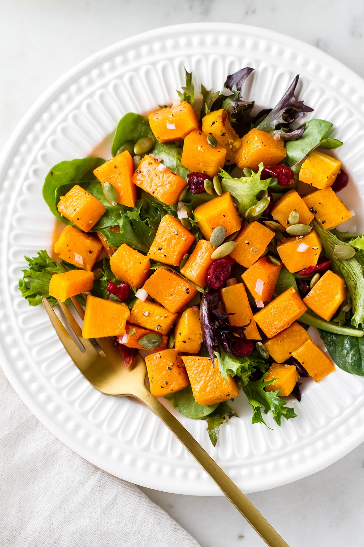top down view of a small white plate with serving of butternut squash salad with gold fork.