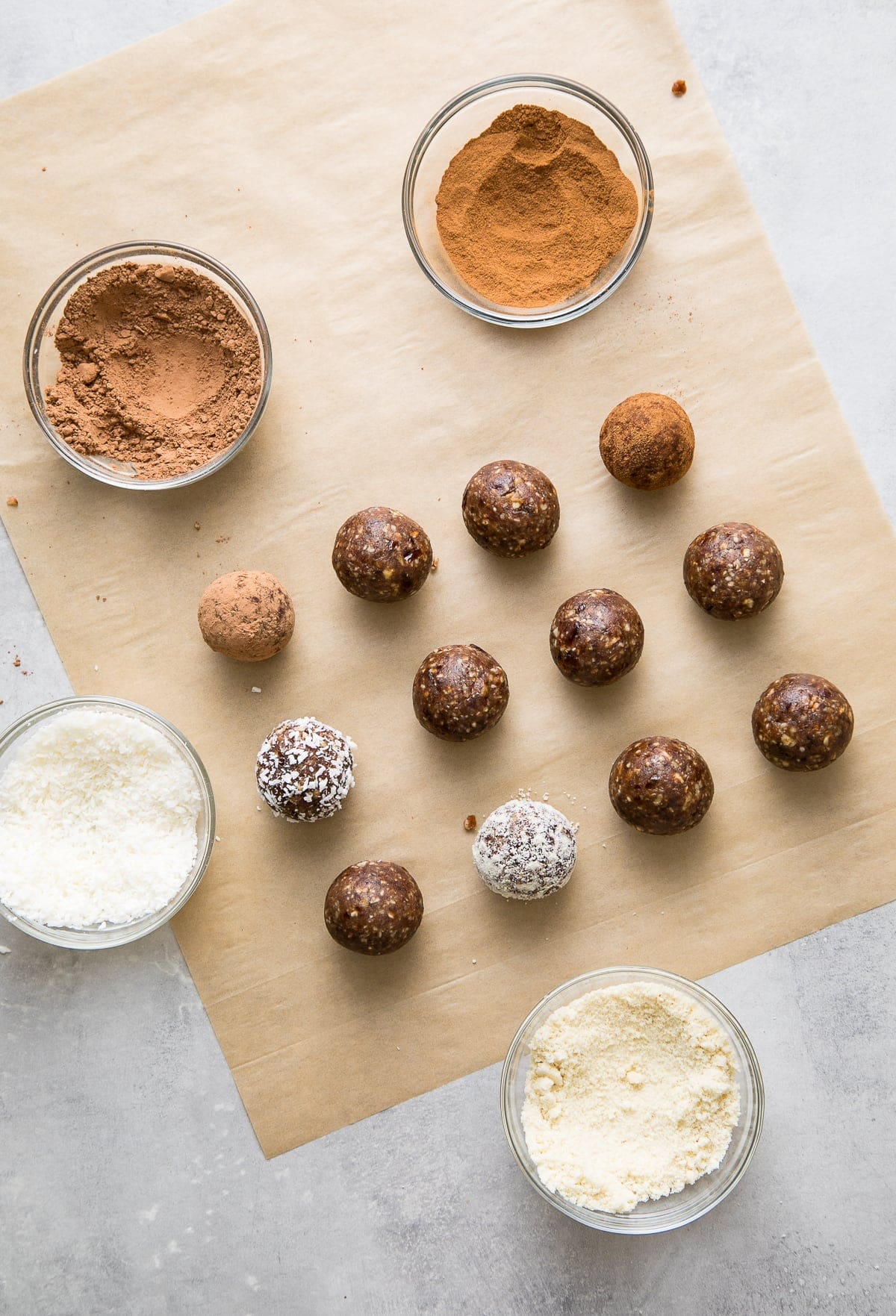 top down view showing the process of rolling energy balls in cocoa, cinnamon and coconut.