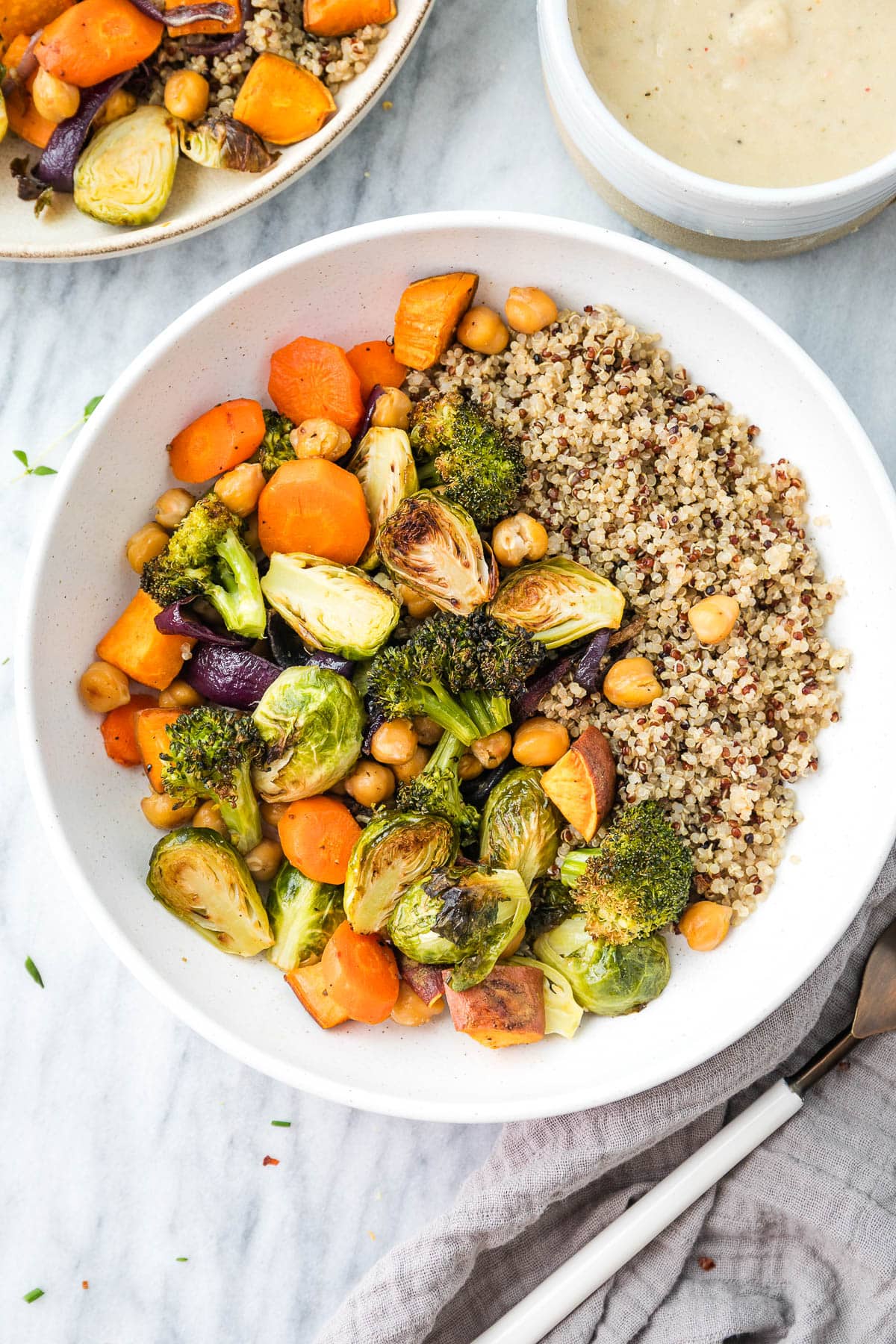 top down view of roasted veggies with quinoa in a bowl with white bean sauce in a gravy bowl.