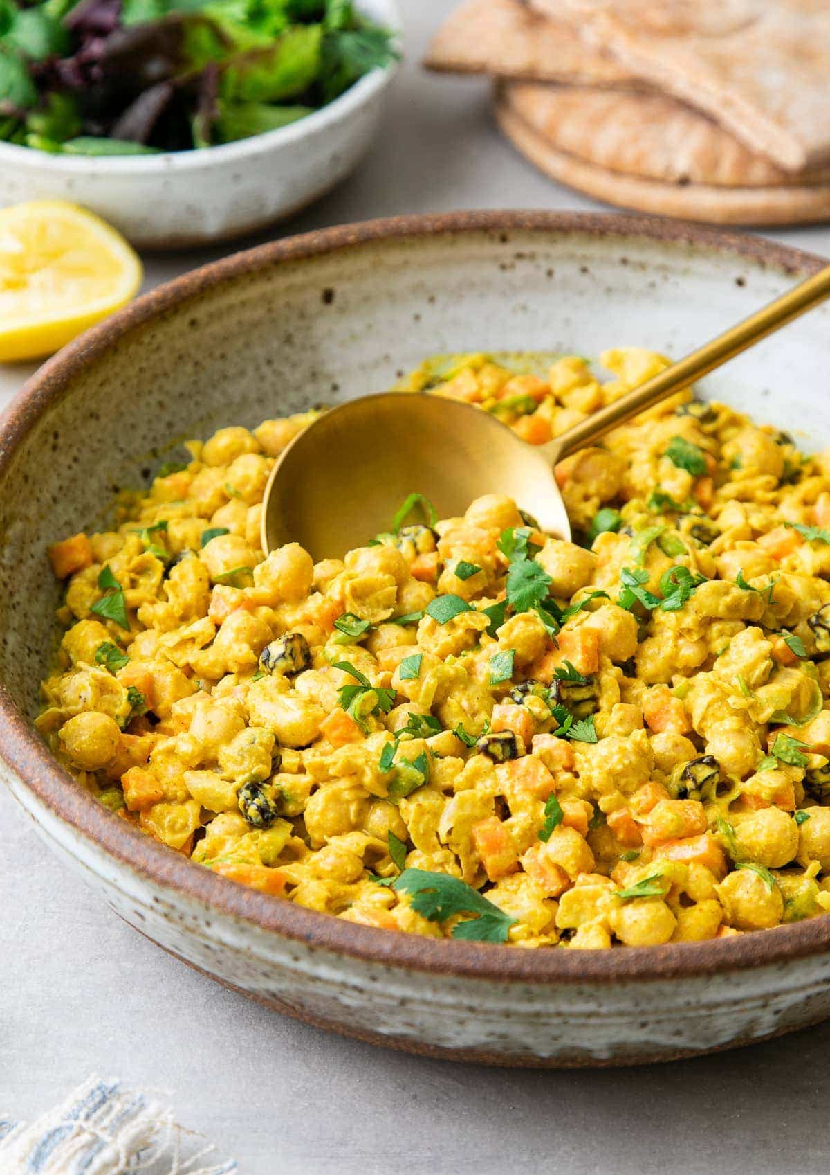 side angle view of bowl with freshly made healthy curried chickpea salad with serving spoon.