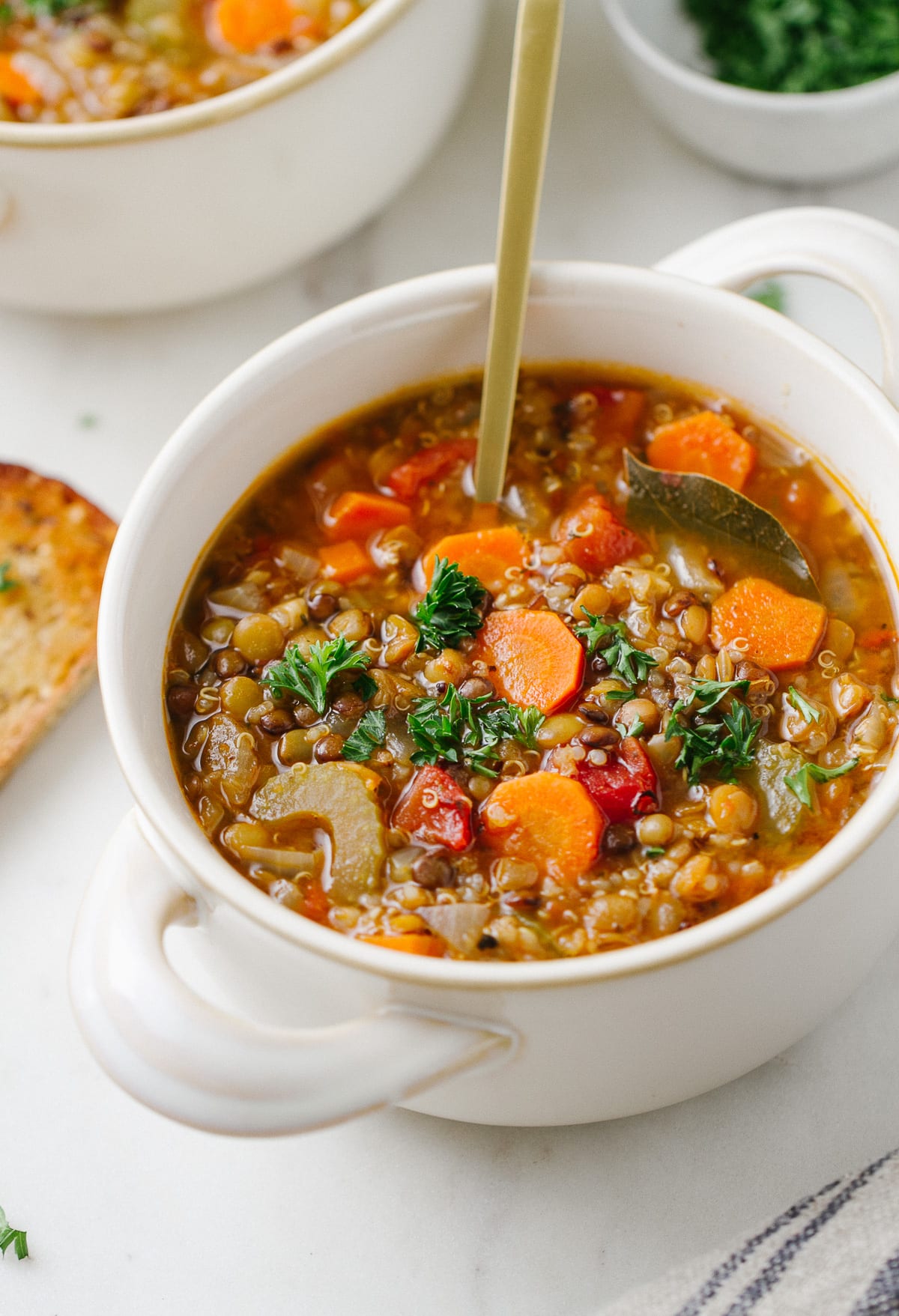 side angle view of a bowl with a serving of healthy smoky lentil and quinoa soup with spoon.