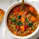 top down view of a bowl with a serving of healthy smoky lentil and quinoa soup with spoon.