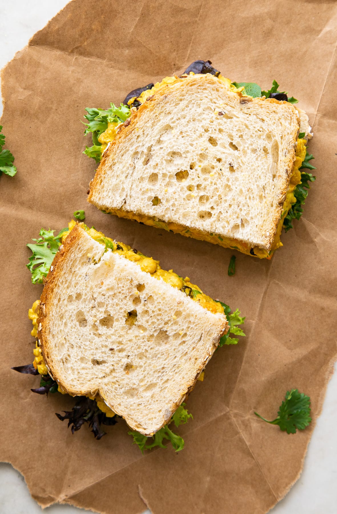 top down view of curried chickpea salad sandwich sliced in half on flat surface.