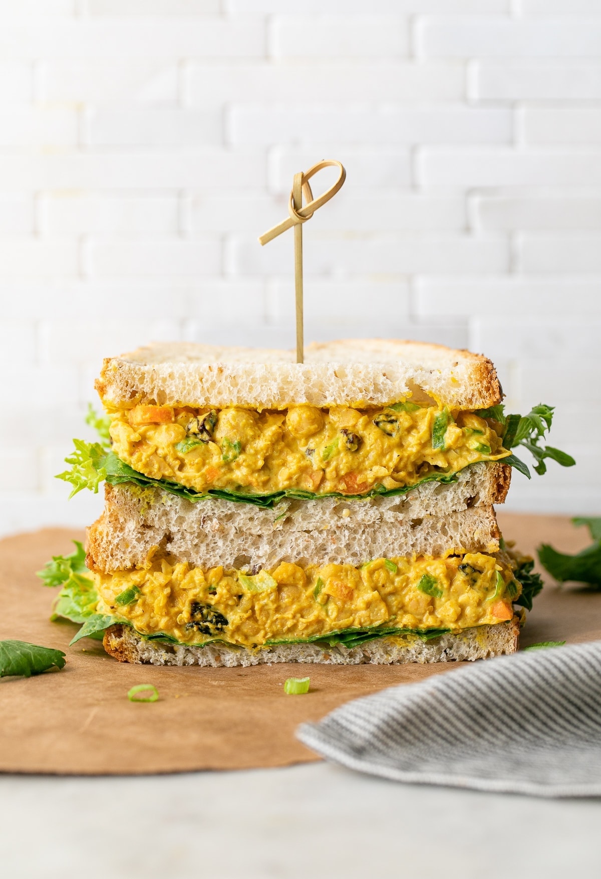 head on view of curried chickpea salad sandwich sliced in half and stacked.