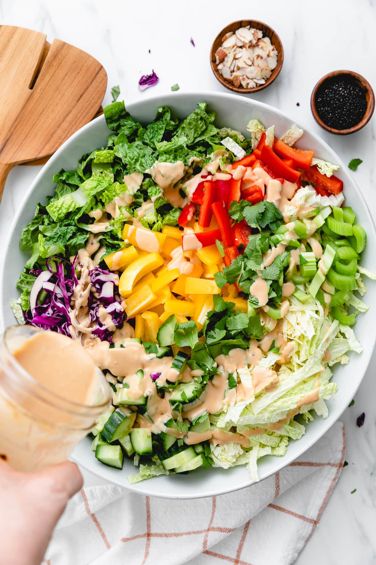 top down view of ingredients for Asian chopped salad in a bowl with peanut dressing being poured over top.