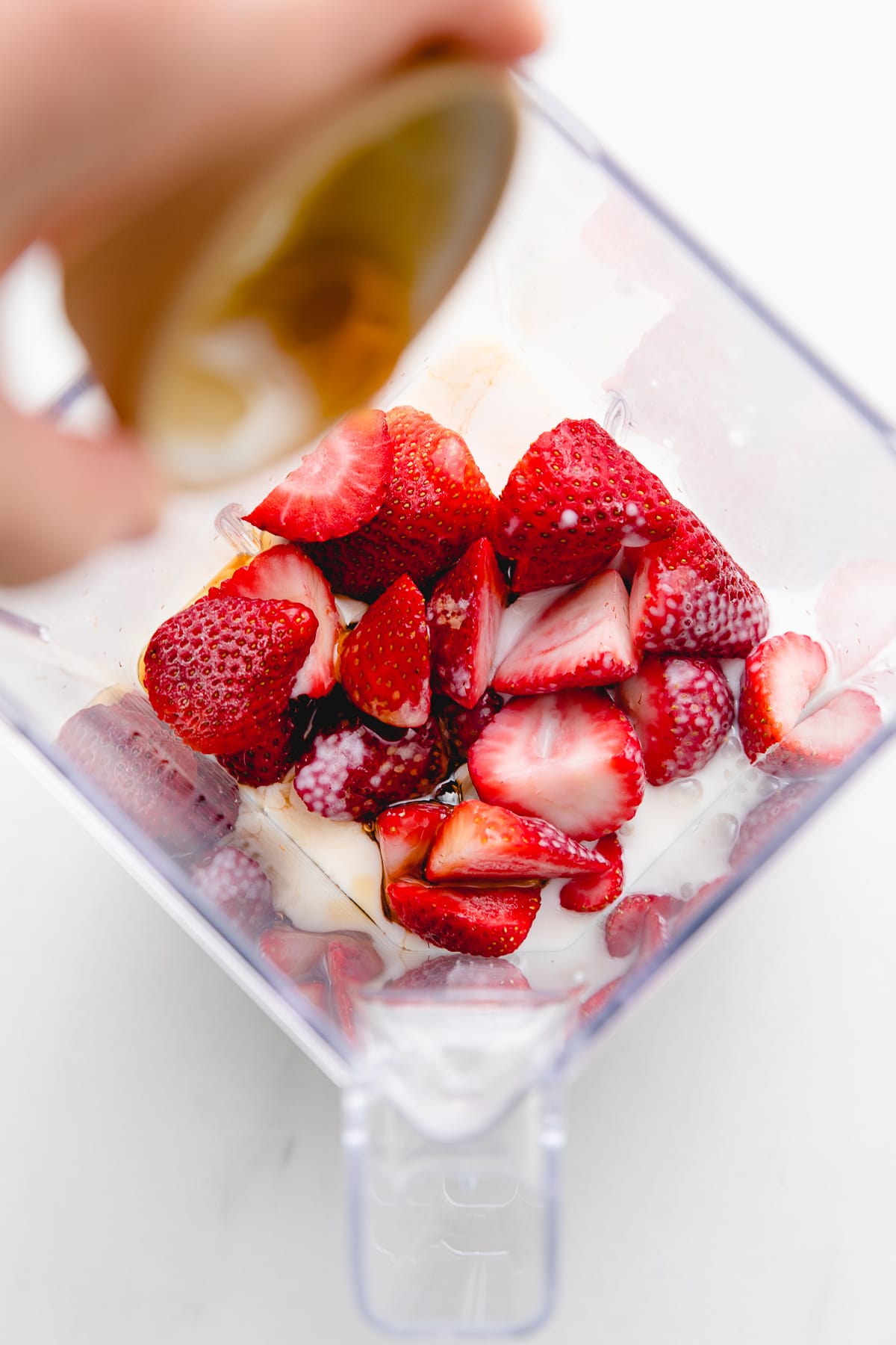 top down view of blender cup with strawberry shake ingredients added.