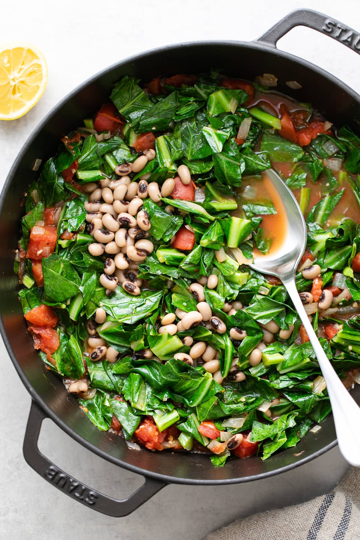 top down view of freshly made vegan collard greens in a pan with beans and a spoon.