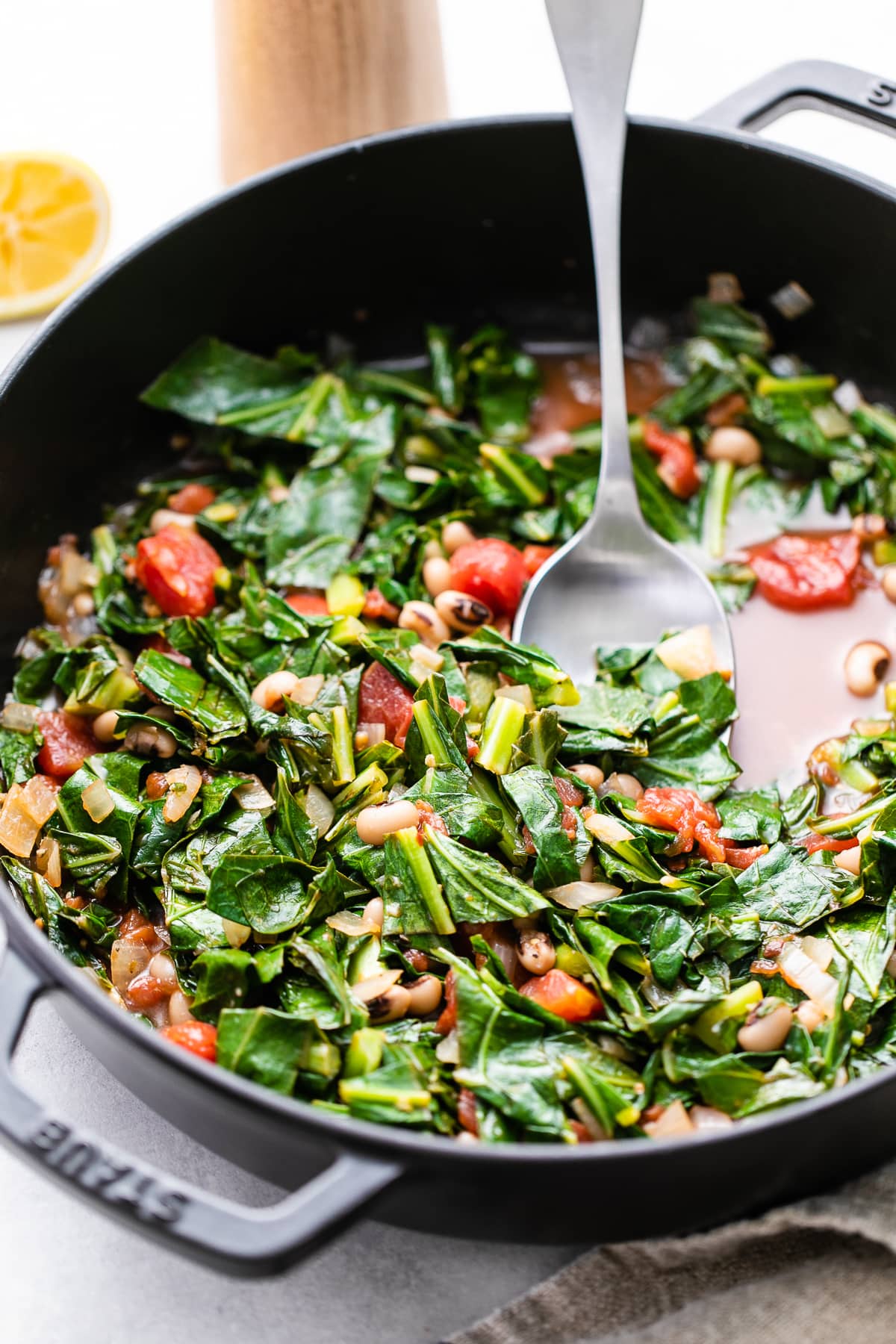 side angle view of freshly made vegan collard greens in a pan with spoon.